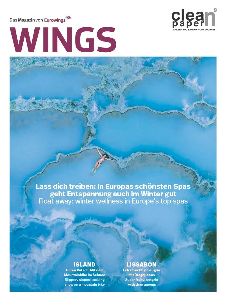 Magazine cover titled 'WINGS' from Eurowings, featuring an aerial view of a hot spring or geothermal area with a person floating in the water. Text highlights winter wellness and spa destinations in Europe, including Island for mountain biking in snow and Lisbon for sangria.