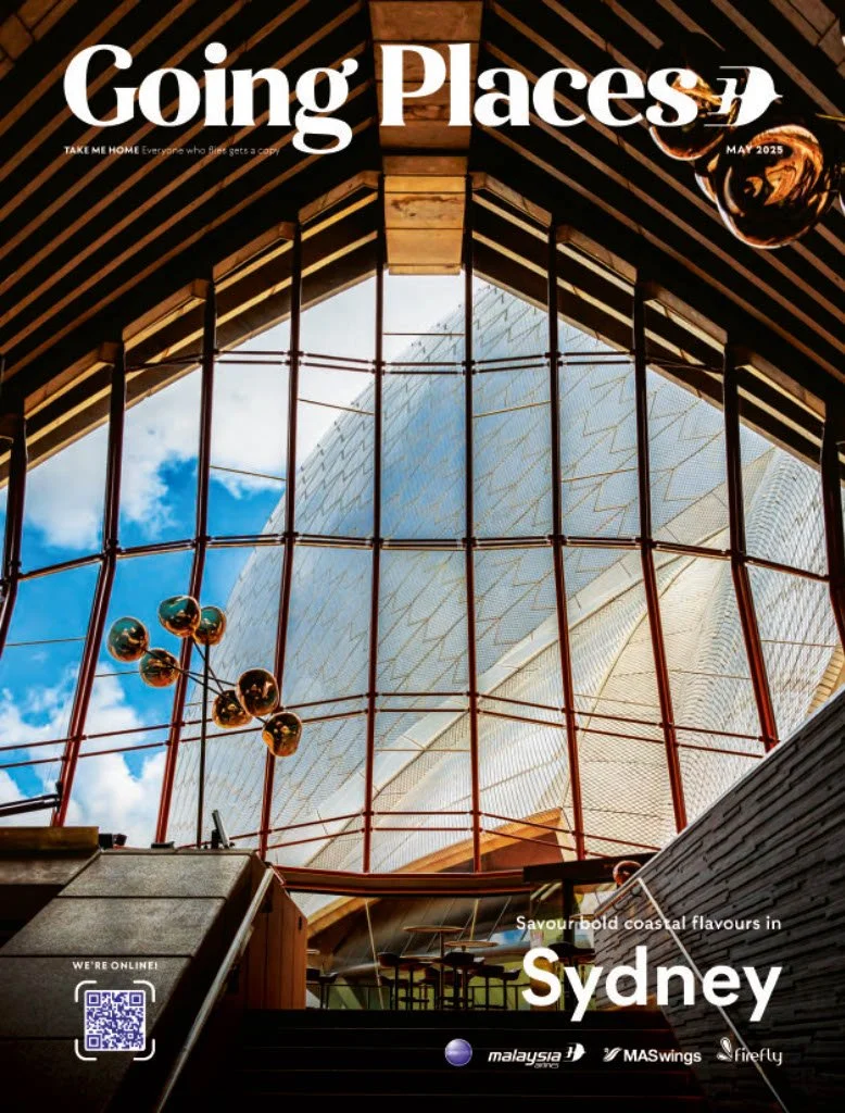 Cover of Going Places magazine featuring an interior view of a modern building with a large glass window showing the Sydney Opera House against a blue sky, with text promoting travel in Sydney, Australia.