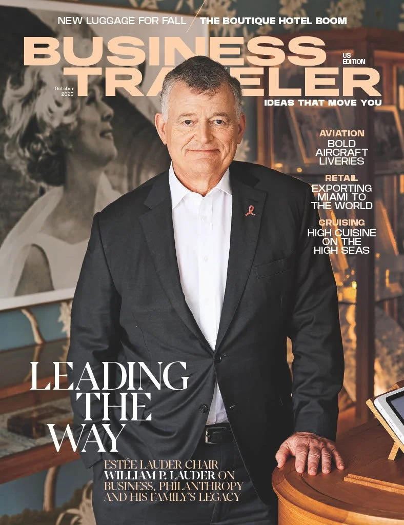 Cover of Business Traveler magazine featuring a man in a black suit with a white shirt, standing in front of a bookcase. The cover highlights topics like luggage, business ideas, aviation, retail, and cruising.