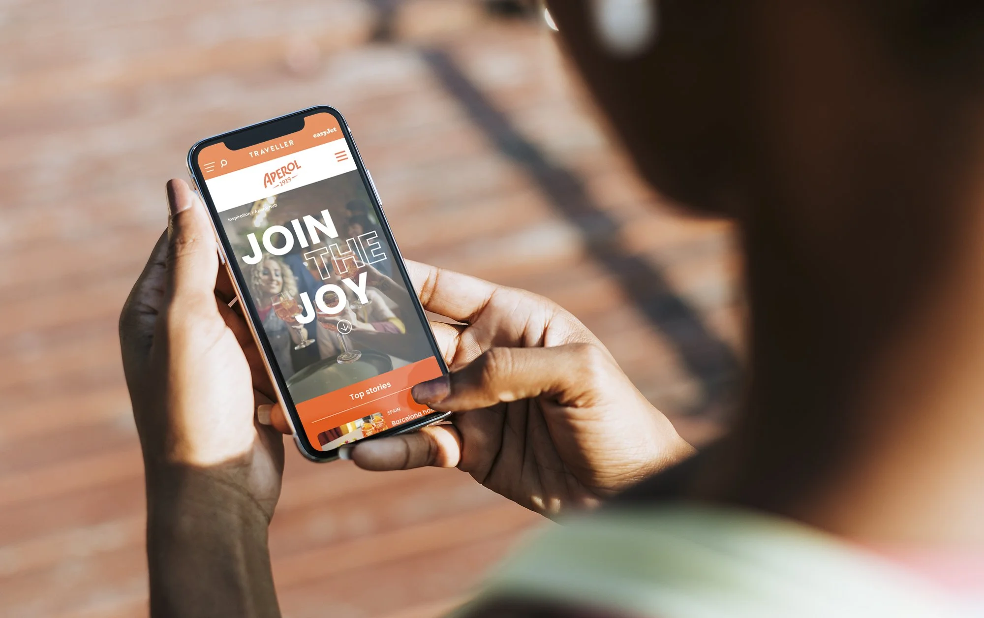 Person holding a smartphone with a webpage displaying the message 'Join the Joy' and an image of smiling women at a table.