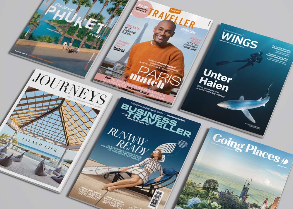 Six travel magazines arranged in a fan pattern, featuring covers with images of tropical locations, a man in an orange sweater, a diver and a shark, and a woman relaxing on a deck chair.