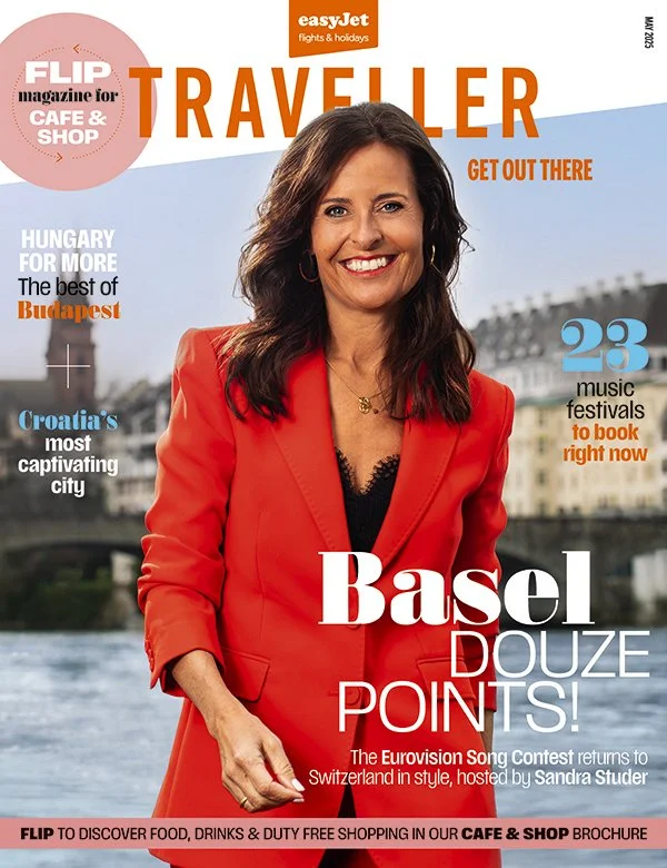 Magazine cover featuring a woman in a red blazer smiling, with text about travel destinations, Hungary, Budapest, Croatia, music festivals, and the Eurovision Song Contest.