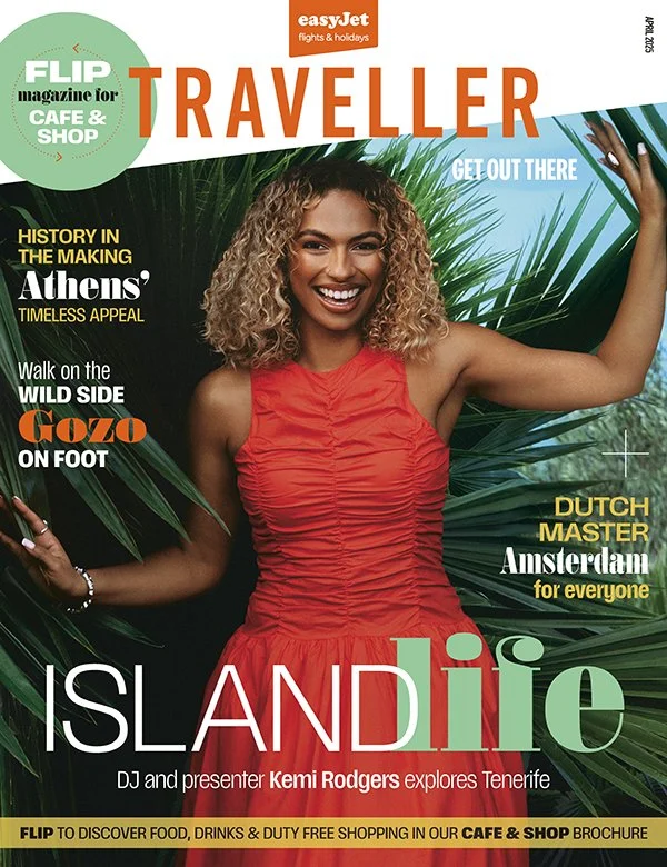 The cover of a travel magazine titled "TRAVELLER" featuring a smiling woman with curly blonde hair in an orange dress, holding large tropical palm leaves, with various article headlines about Athens, Gozo, and Amsterdam, and the magazine promotes travel to Tenerife.