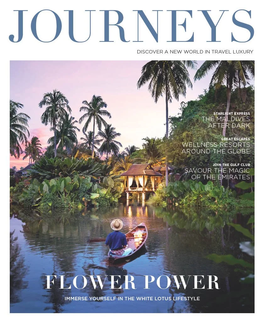 A person in a boat on a river surrounded by lush tropical vegetation and palm trees during sunset, with a traditional hut on stilts in the background.