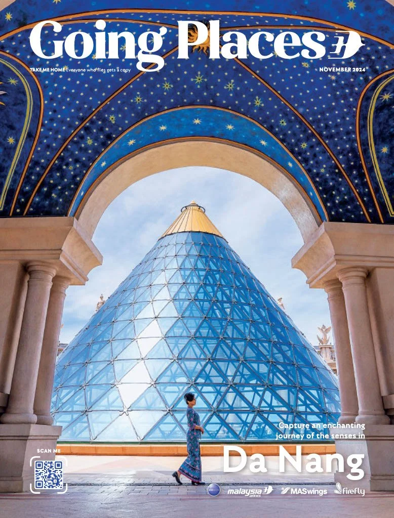 Cover of Going Places magazine featuring a glass pyramidal structure at a temple in Da Nang, Vietnam, with an arch and columns in the foreground. A woman in traditional dress walks in front of the structure.