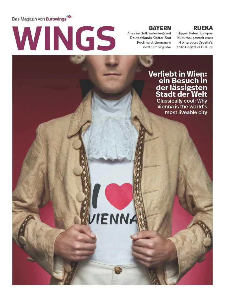 Cover of WINGS magazine featuring a woman dressed in historical costume with a modern I love Vienna T-shirt underneath. The background is a gradient red. Text highlights articles about Bayern and Rijeka, travel and cultural topics.