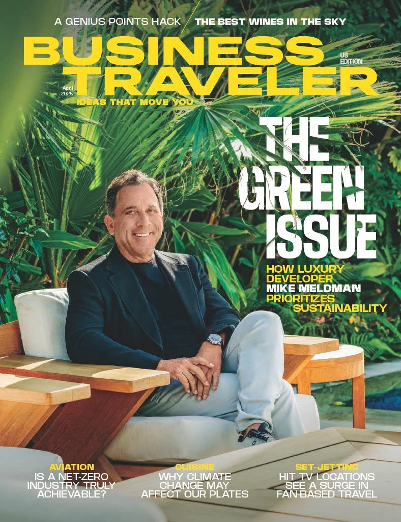 Cover of Business Traveler magazine featuring a man sitting outdoors among lush green tropical plants, smiling, with magazine headlines about sustainability, luxury development, aviation, cuisine, and travel.