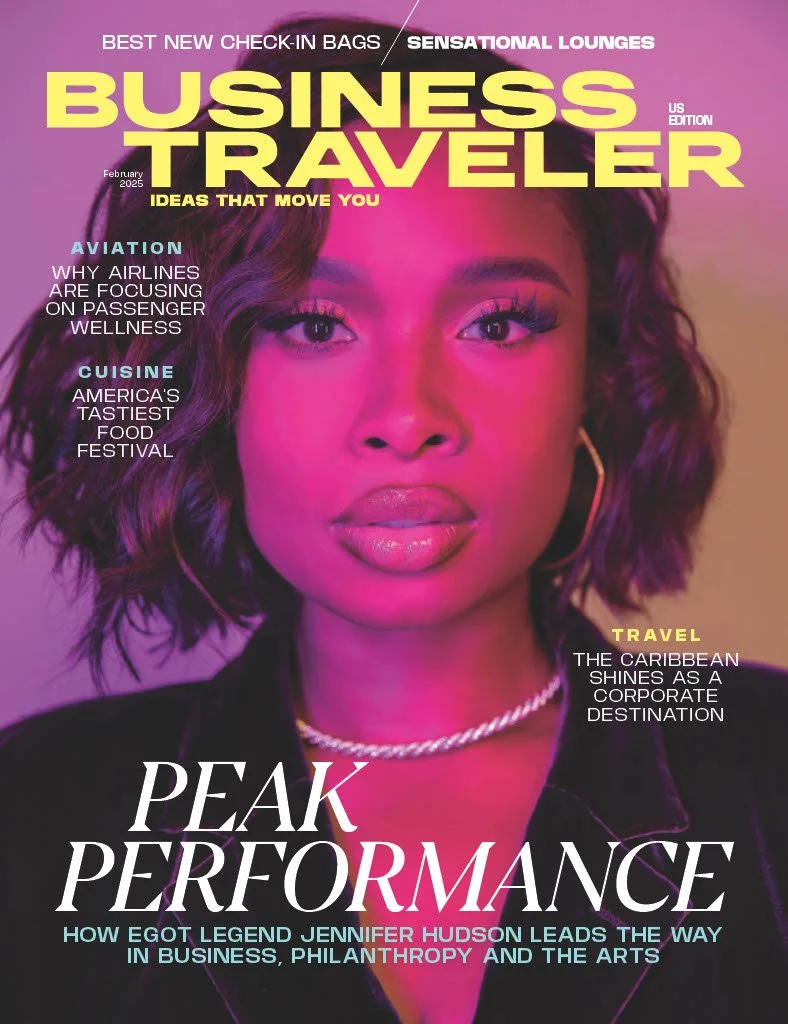 Cover of Business Traveler magazine, February 2025 issue, featuring a close-up of a woman with dark curly hair, wearing a black blazer, gold hoop earrings, and a chain necklace, with text highlighting travel, cuisine, aviation, and business topics.