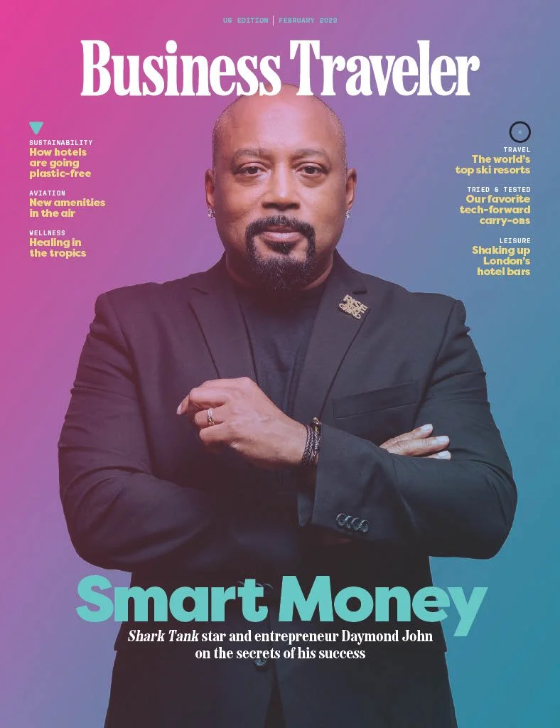 The cover of Business Traveler magazine featuring entrepreneur Daymond John with a gradient purple and blue background. Headlines include topics on sustainability, aviation, wellness, travel, tech, and leisure, with a focus on money and success.