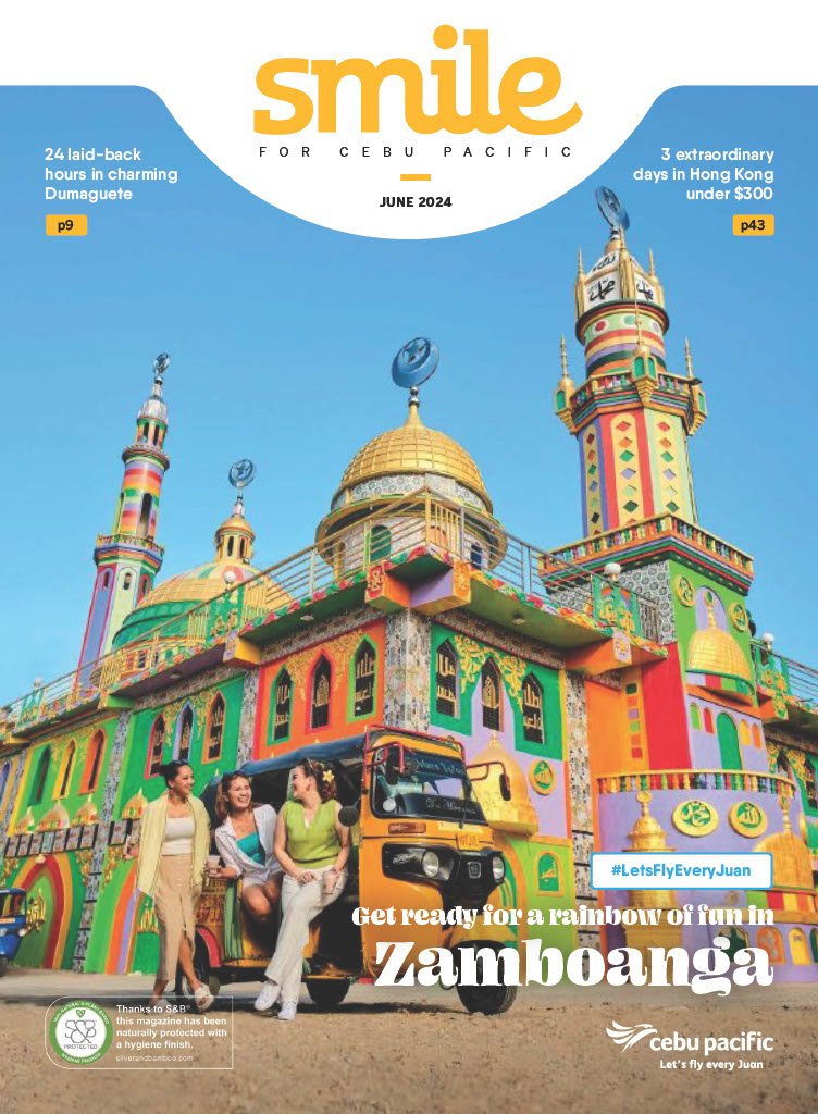 Colorful and vibrant building decorated to look like a rainbow, featuring minarets, domes, and intricate patterns. Three women stand beside a bürn, with a clear blue sky overhead, promoting Zamboanga with a rainbow theme.