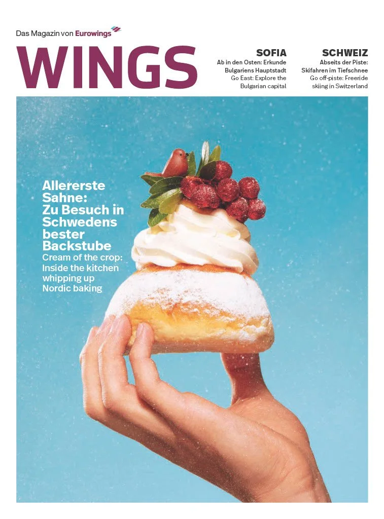 Close-up of a hand holding a piece of pastry topped with cream and berries, against a blue background.