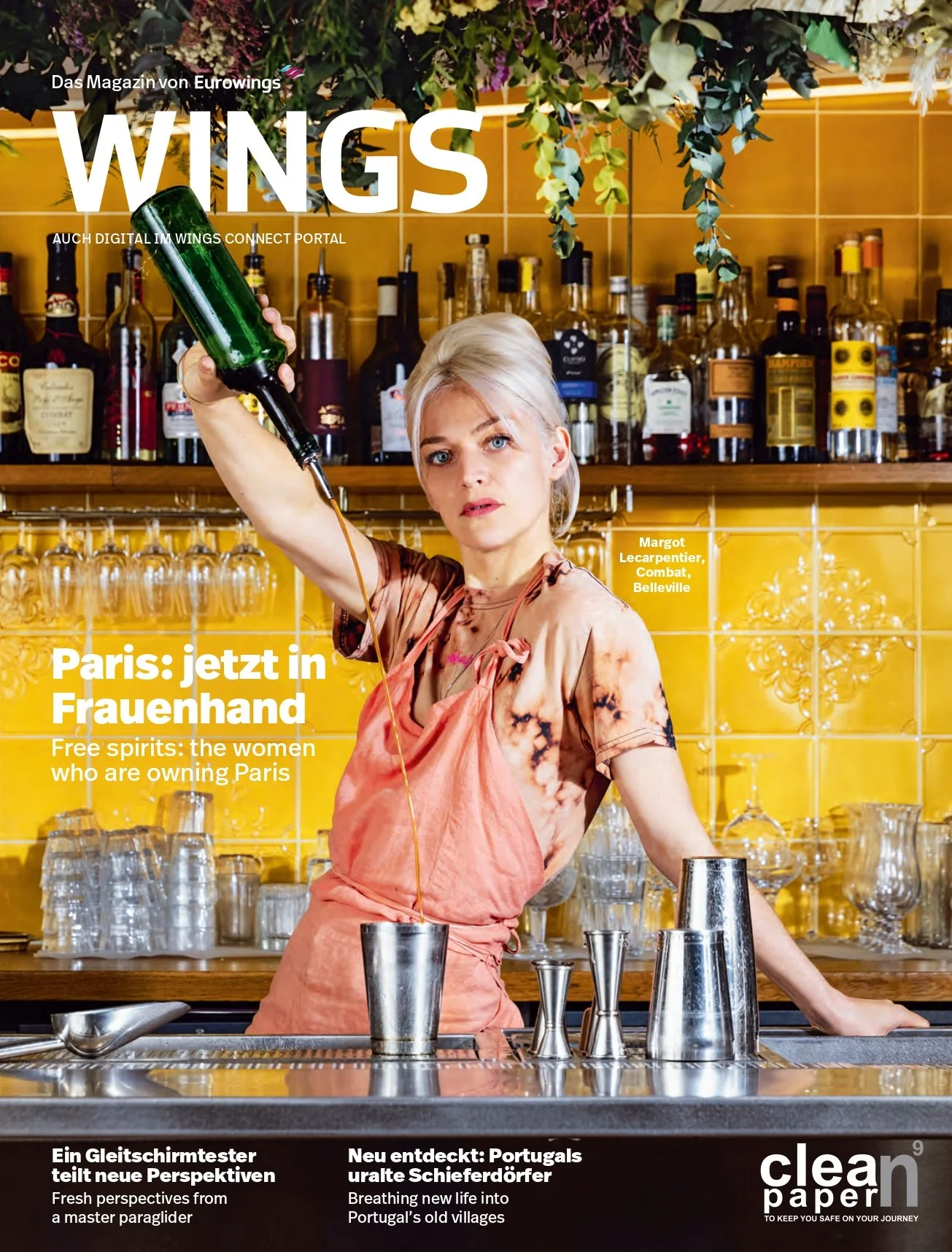 Magazine cover featuring a woman in a bar pouring a drink, with shelves of liquor bottles behind her, yellow tiled wall, and green foliage above.