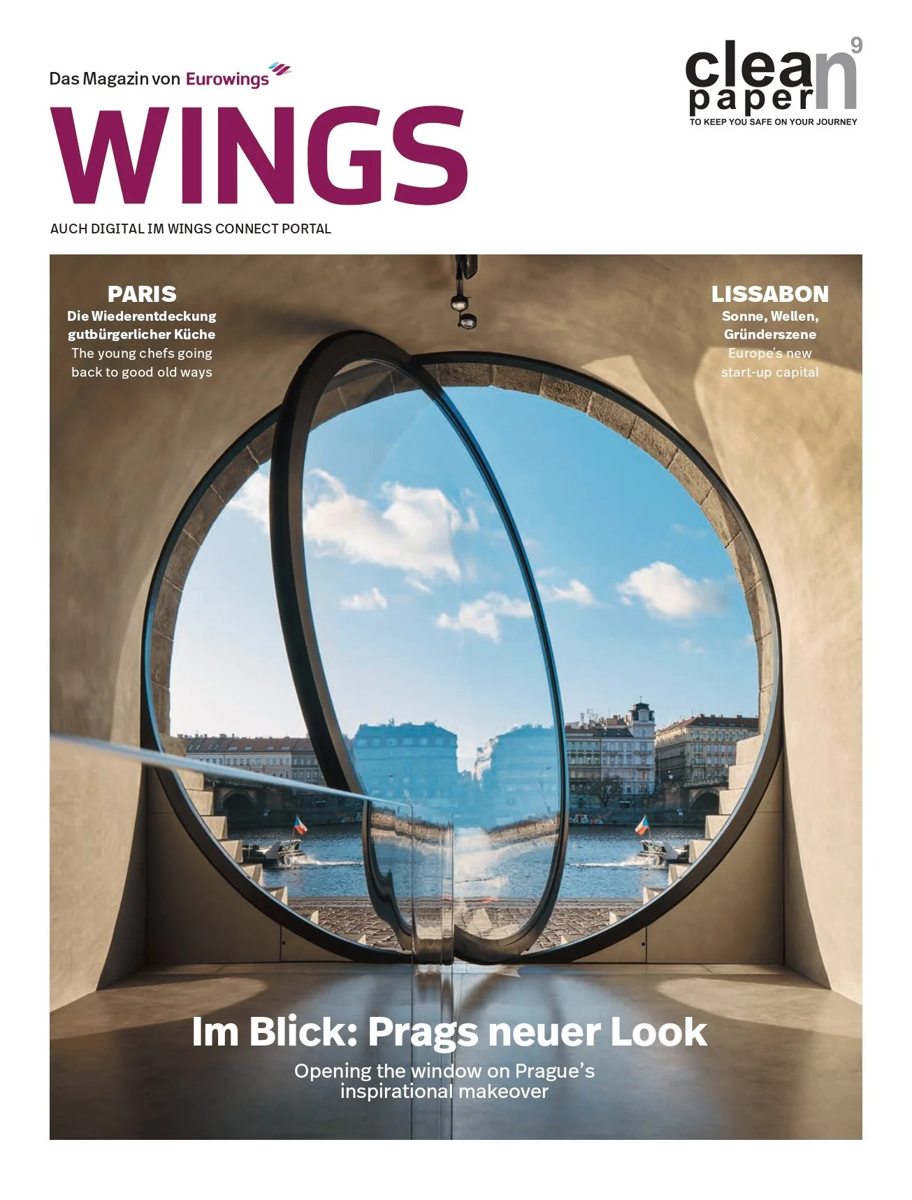 Cover of a magazine titled "WINGS" with a large round window opening onto a view of a river and buildings in Prague, Czech Republic, under a blue sky with some clouds.