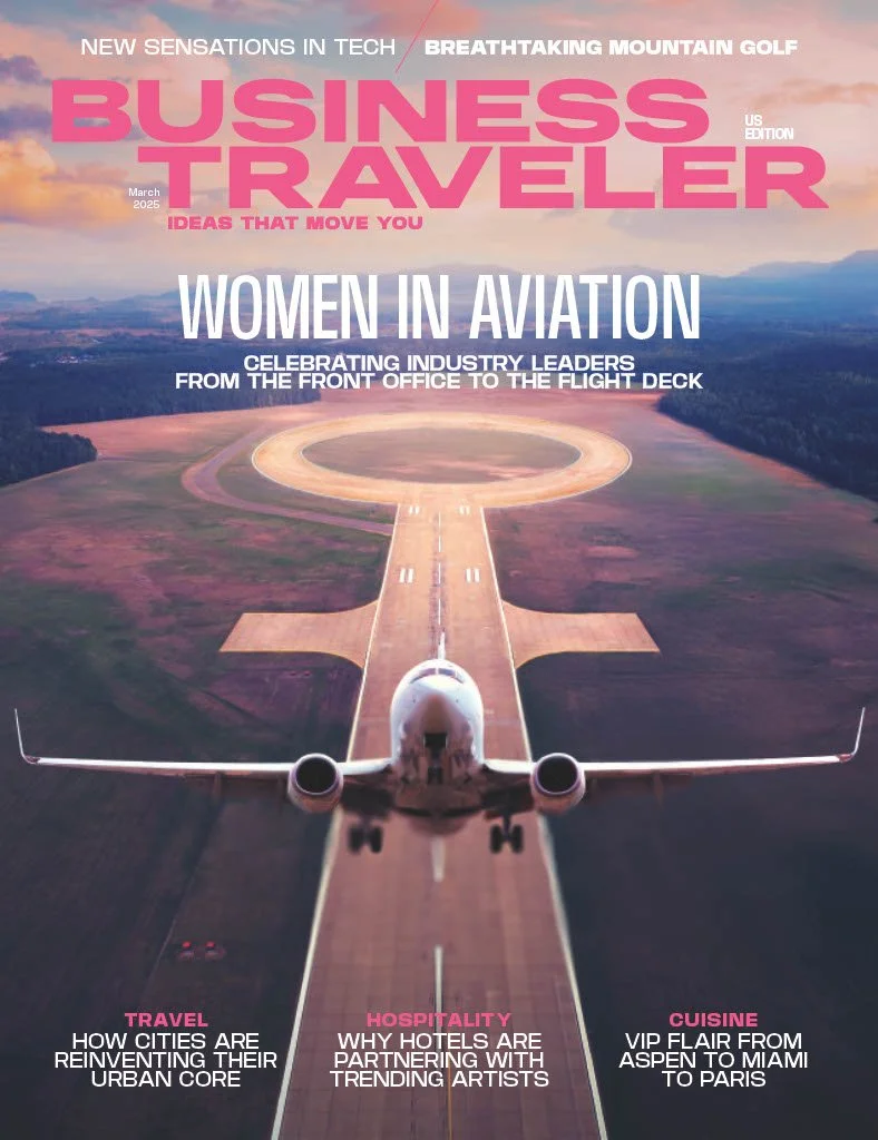 Aerial view of a small private jet on a runway at sunset with hills and clouds in the background. The magazine cover features the title 'BUSINESS TRAVELER' in large pink letters, and headlines about women in aviation, city travel, hotel partnerships, and cuisine.
