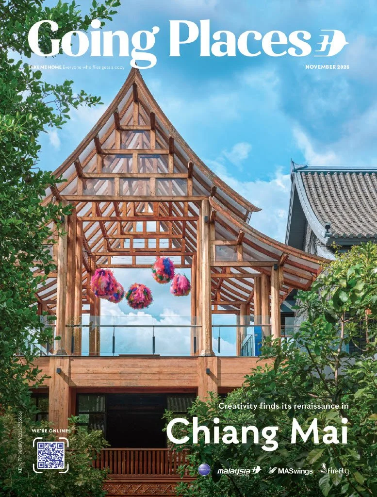 Cover of 'Going Places' magazine featuring a wooden traditional Thai-style building under a blue sky with some clouds, surrounded by green trees, and colorful hanging decorations inside the structure, with text indicating a focus on Chiang Mai in November 2025.