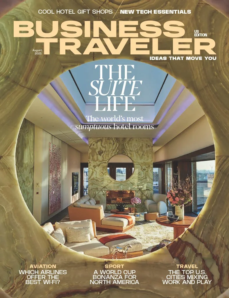 Interior of a luxury hotel suite with a modern, stylish living area featuring a fireplace, large windows, and decorative flowers, viewed through a circular sculpture or frame.