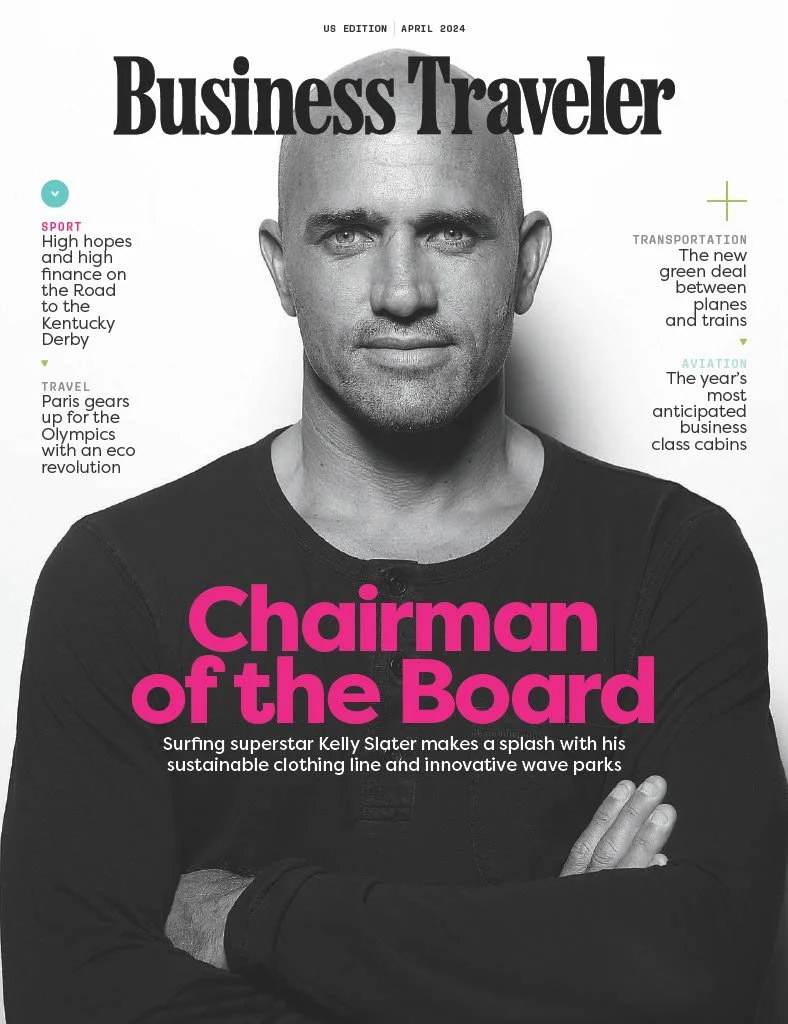 Cover of Business Traveler magazine, April 2024 edition, featuring a black and white portrait of Kelly Slater with text highlighting topics like sports, travel, transportation, and aviation, and with bold pink text that states "Chairman of the Board".
