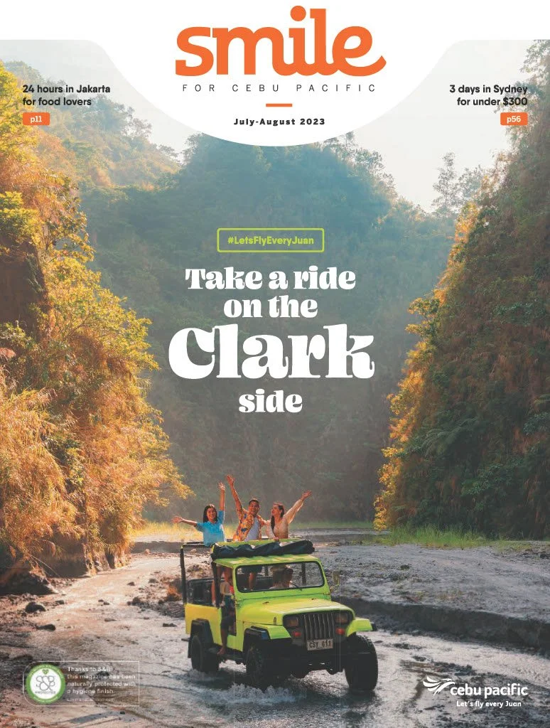 Travel magazine cover titled 'Smile for Cebu Pacific', July-August 2023. Features a photo of three women joyfully riding on top of a green jeep in a river surrounded by lush mountains. Headlines highlight travel destinations in Jakarta, Sydney, and Clark.