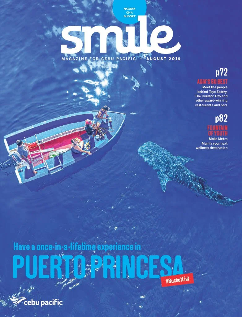 Magazine cover titled 'Smile' for Cebu Pacific, August 2019, featuring an aerial view of a small boat with several people on it, and a large whale shark swimming underneath in the ocean, promoting a trip to Puerto Princesa.