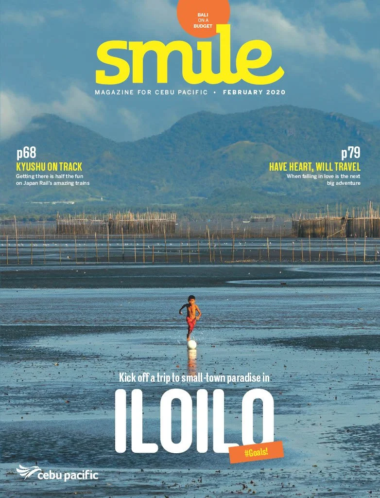 A child running across a shallow water area in Iloilo with mountains in the background, depicted on the cover of a Cebu Pacific magazine titled 'Smile' from February 2020.
