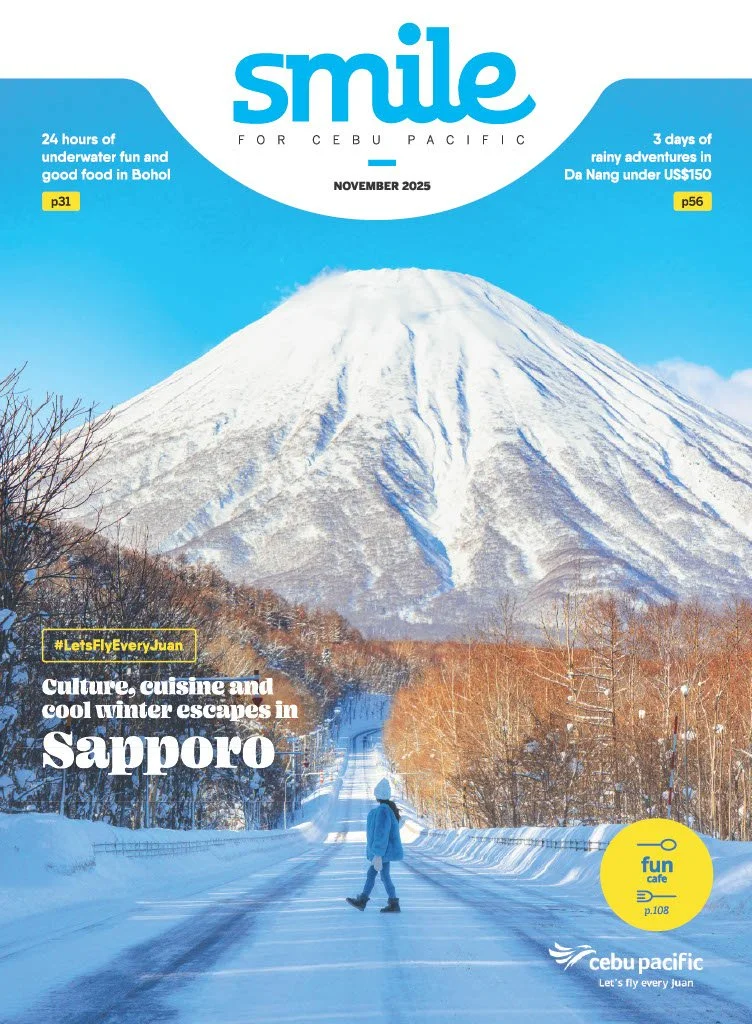 A person in winter clothing walking across a snowy road with a snow-capped mountain in the background during daytime.