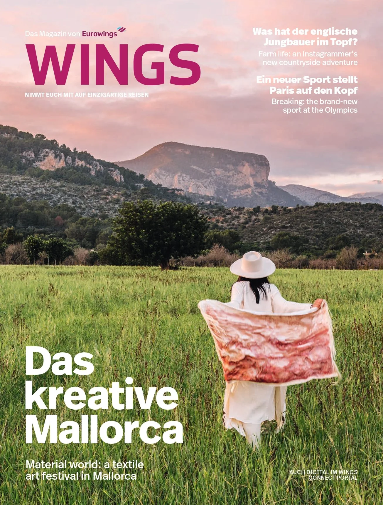 A woman wearing a white dress and wide-brimmed hat standing in a lush green field, holding a large piece of fabric, with mountains and a pinkish sky in the background.