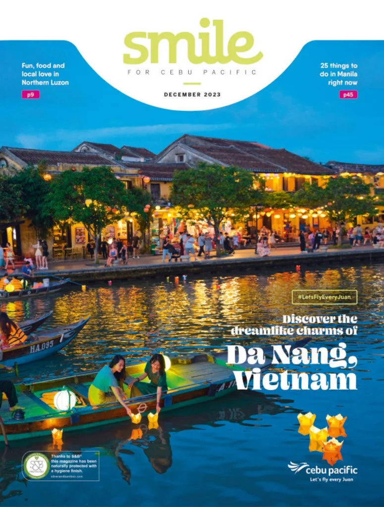 Cover of Cebu Pacific magazine titled "Smile for Cebu Pacific," December 2023 issue, featuring a nighttime waterfront scene in Da Nang, Vietnam, with illuminated boats and a lively street with shops and people with trees along the water.