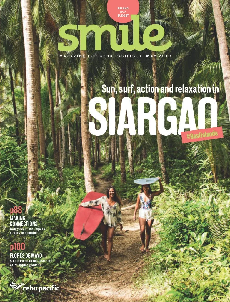 Cover of Smile magazine for Cebu Pacific, May 2019, featuring two women walking on a forest trail with palm trees, carrying surfboards.