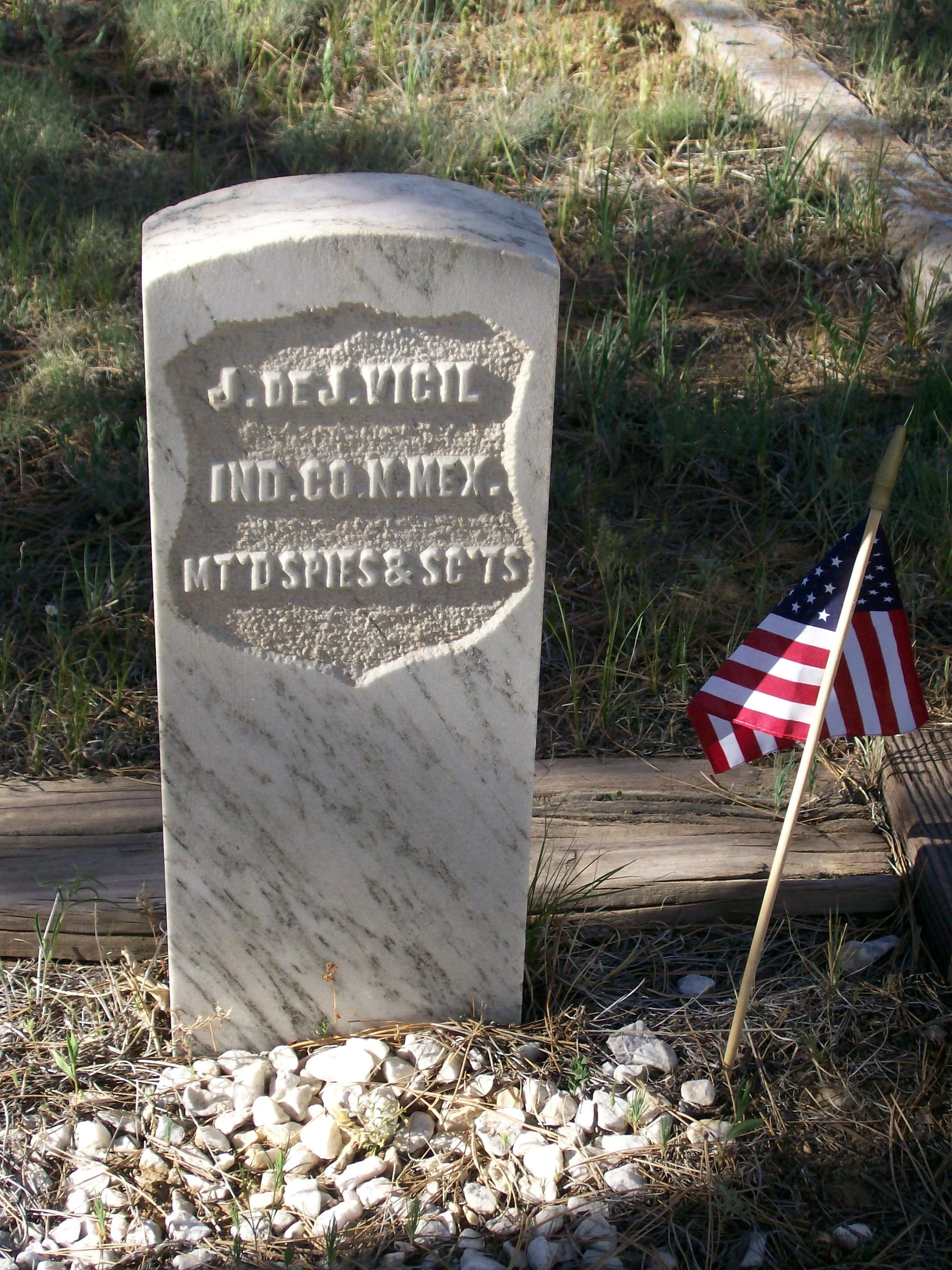 White Marble Gravestone with an american flag next to it. Graveestone reads " J.de J. Vigil, IND.CO.N.MEX., MT'D SPIES & SC'TS