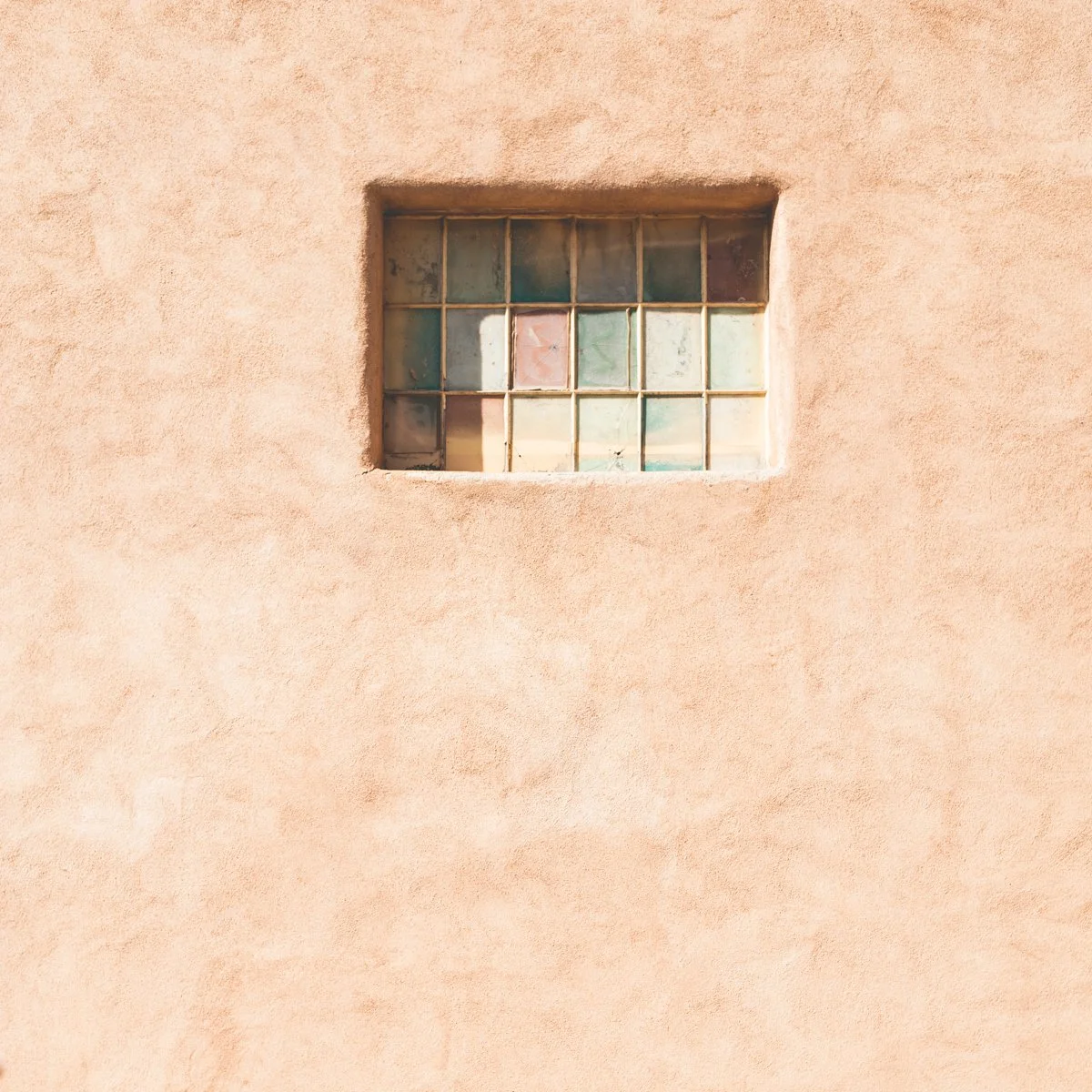 A small window with glass blocks set into a peach-colored stucco wall.