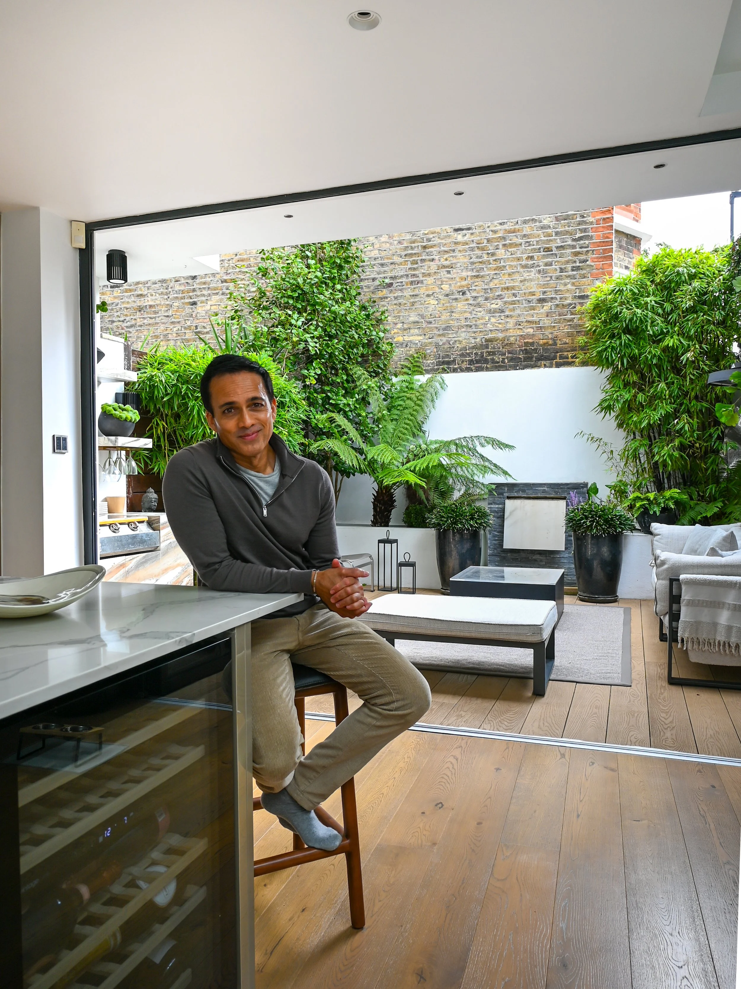 Man sitting at a kitchen island in a modern home with a lush indoor courtyard garden.