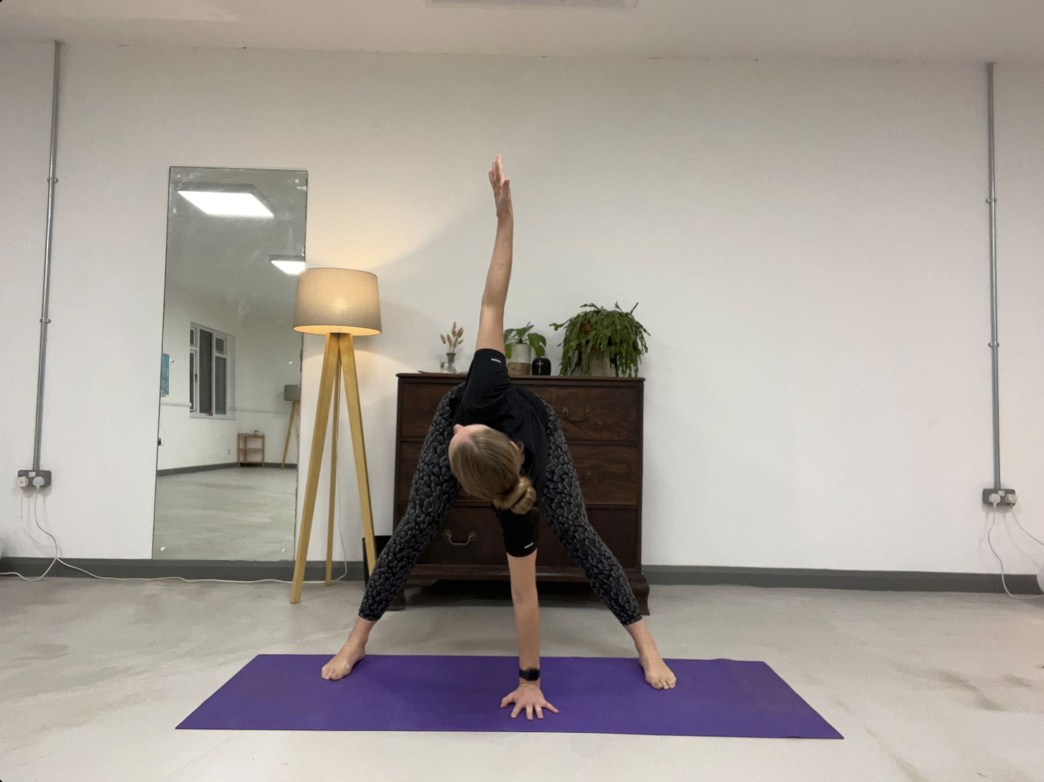A person practicing yoga indoors, performing a pose with one leg extended upward and one hand and foot on the purple yoga mat, while the other hand supports their body.