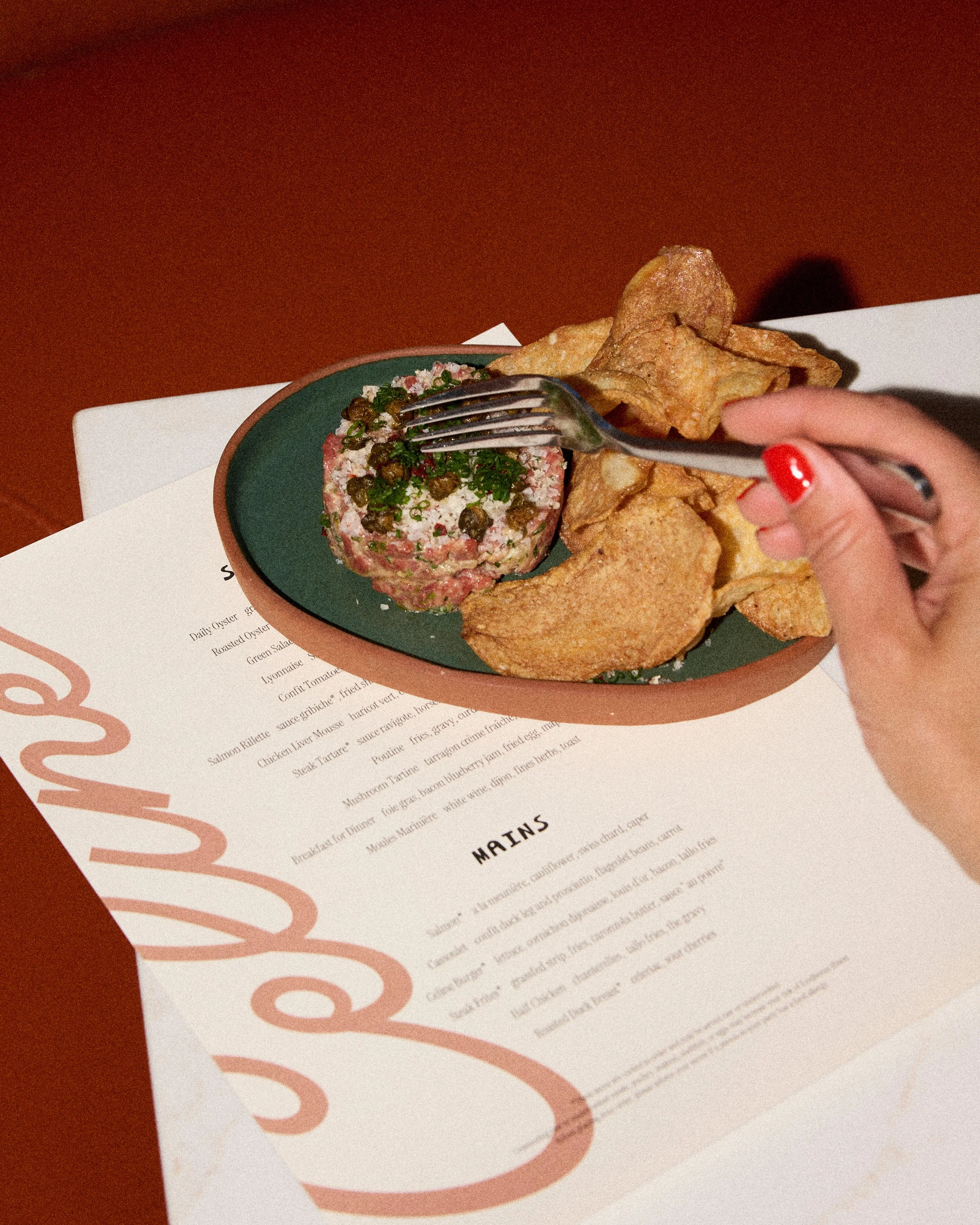 Photo by Emily Kan shows a hand using a fork to start eating steak tartare