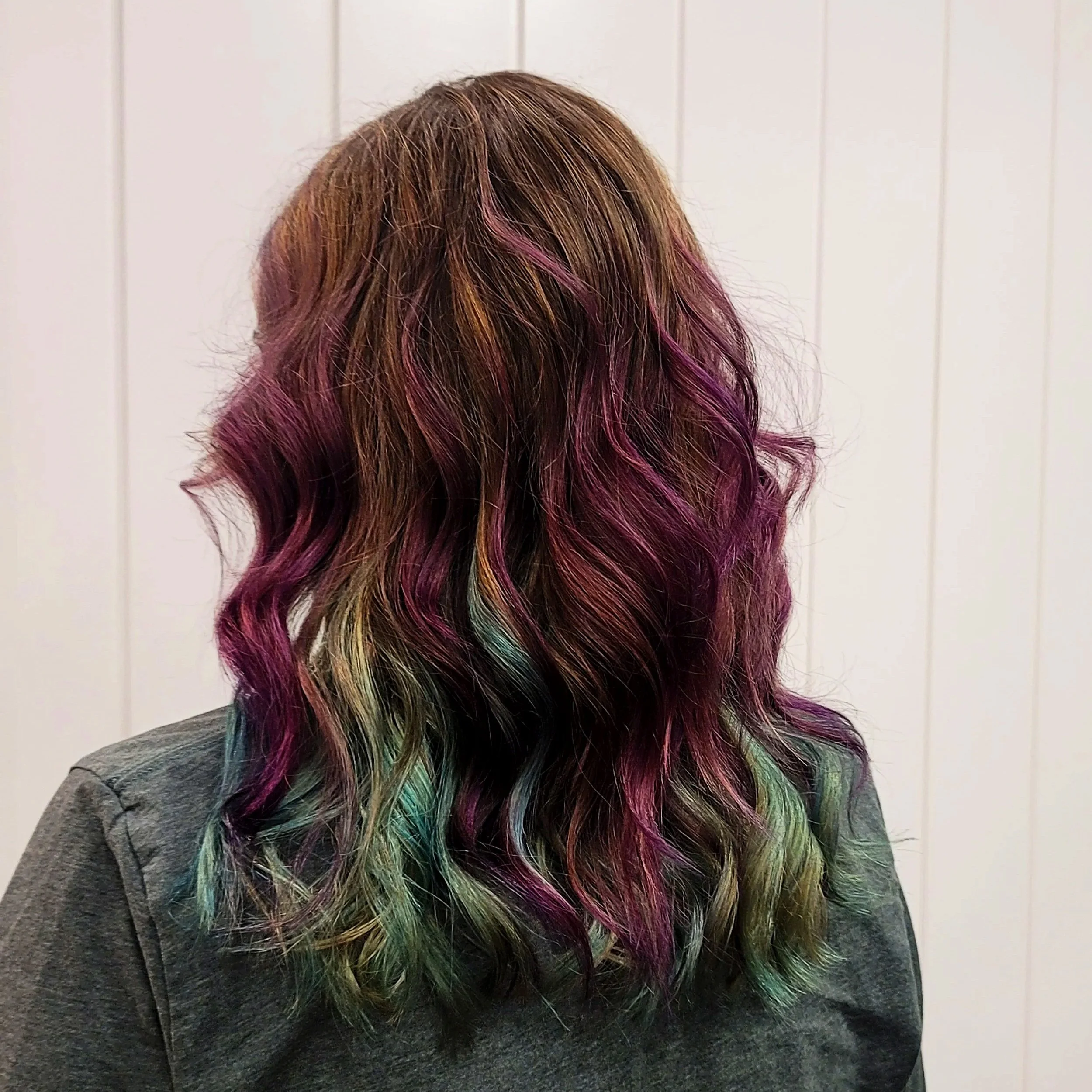 Back view of a woman's wavy hair with multiple vibrant colors including pink, purple, green, and blonde highlights.