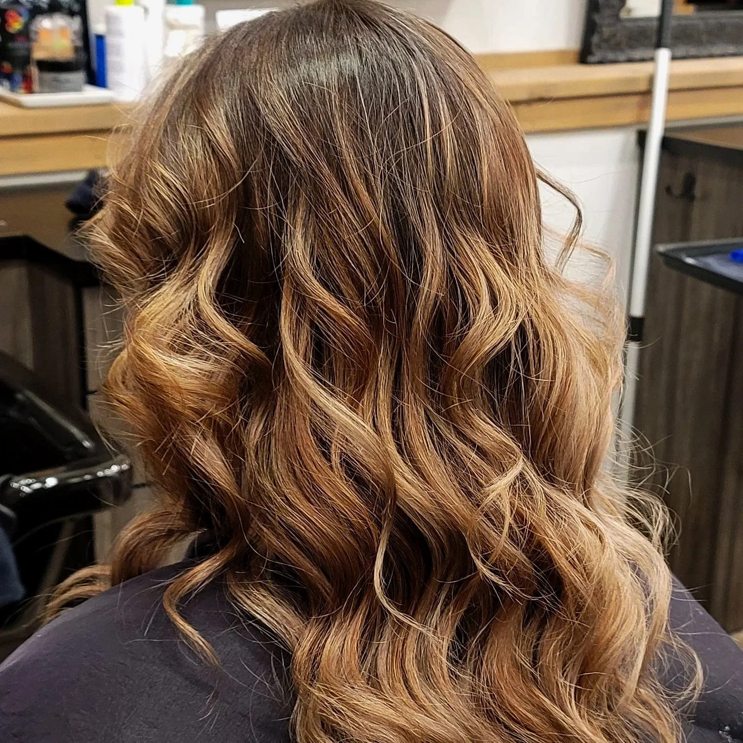 Back of a woman's head with medium-length, wavy, light brown hair in a salon setting.