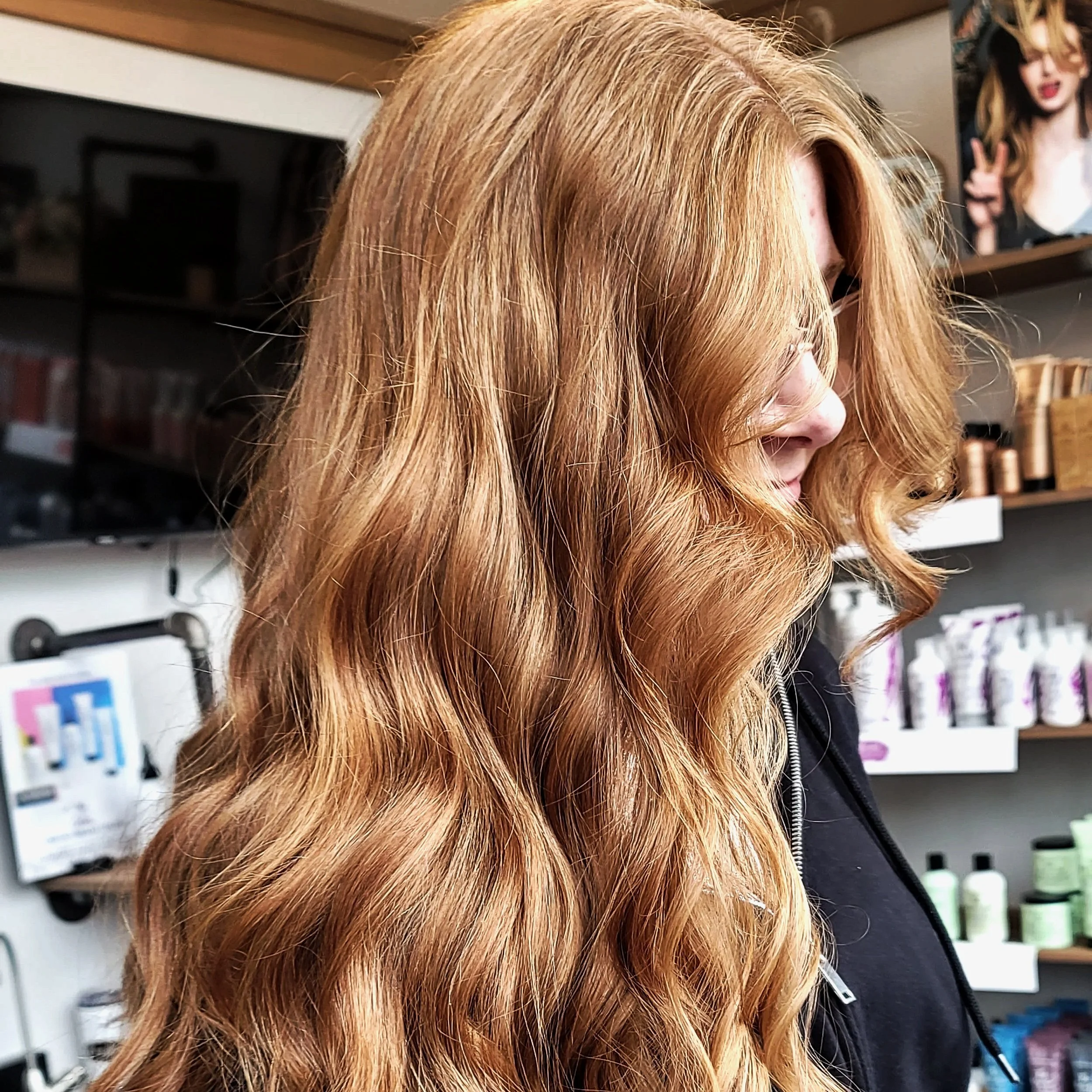 Profile of a woman with long, wavy, red hair inside a store or salon.