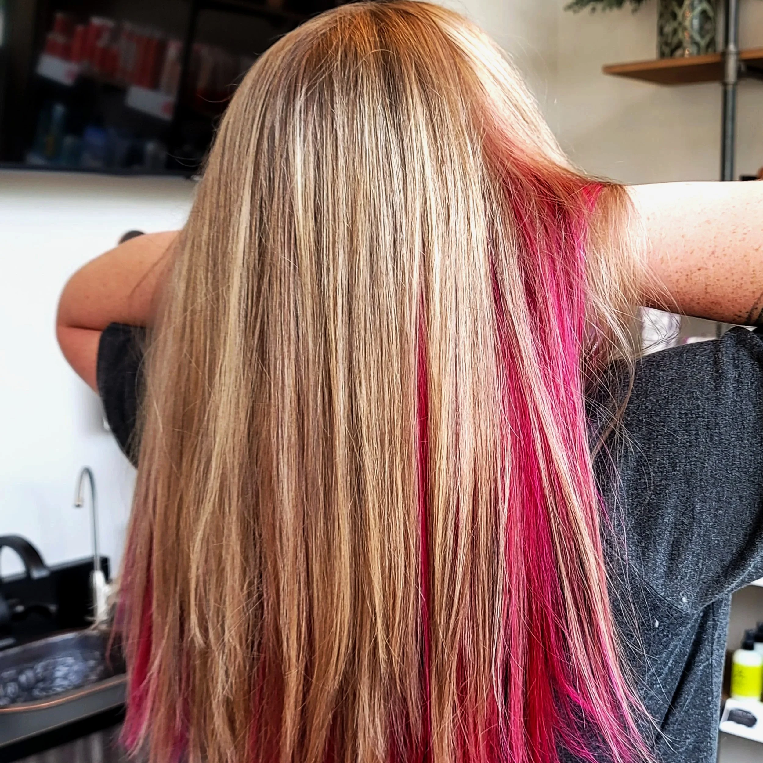 Close-up of a woman with long, straight blonde hair featuring bright pink highlights.