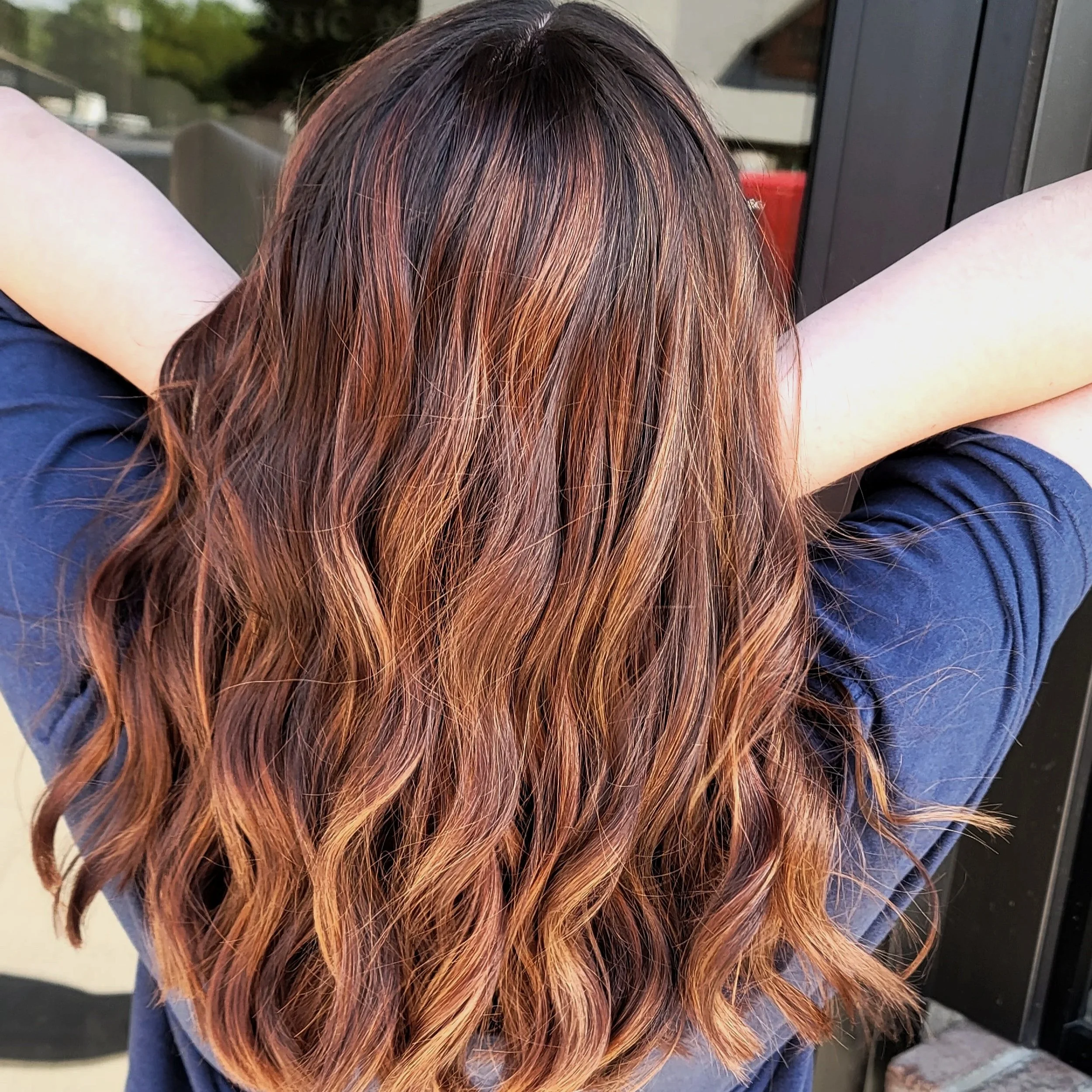 Woman with wavy, multi-tonal auburn hair, wearing a navy blue shirt, extending her arms with elbows bent.