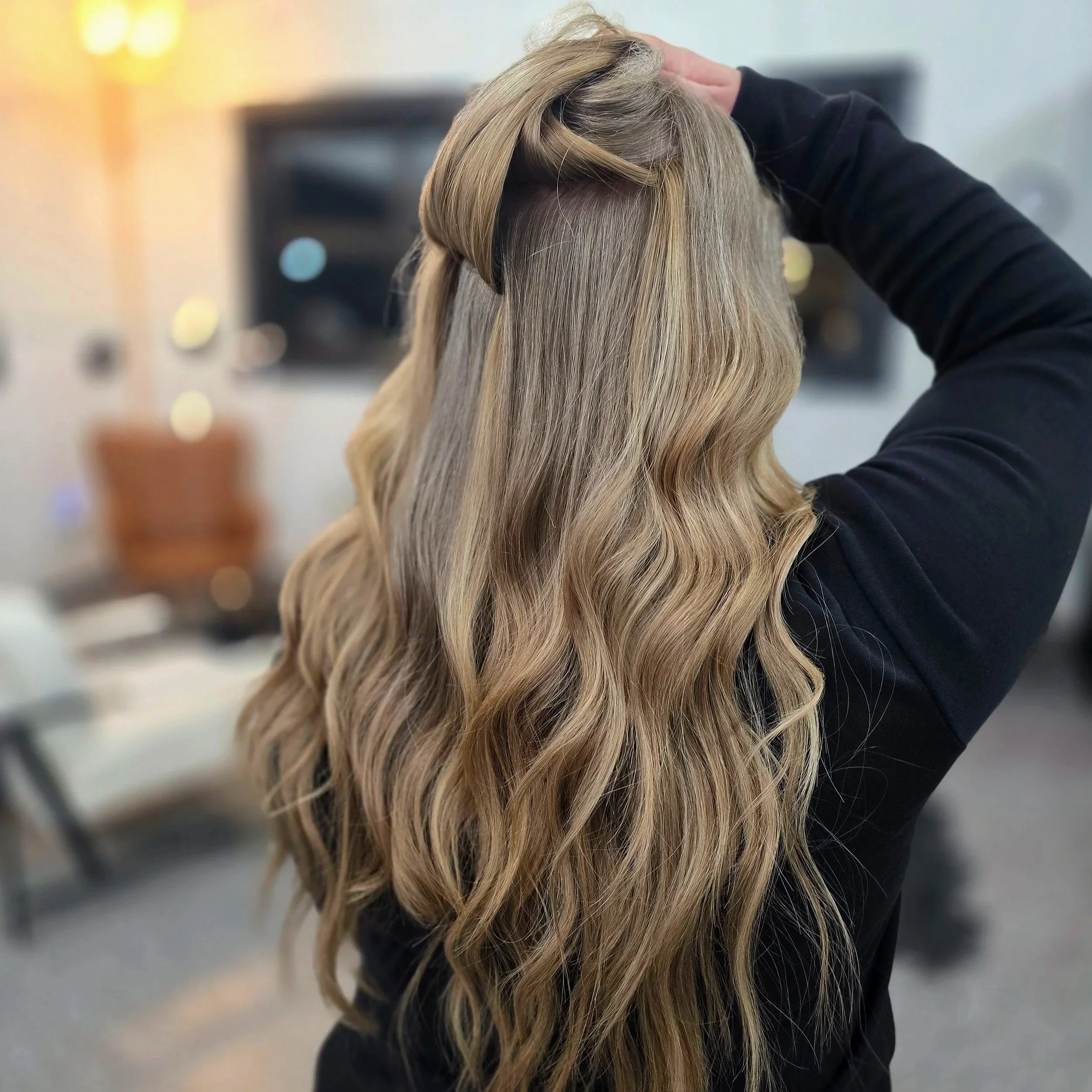 Back of woman with long, wavy blonde hair being styled in a salon.