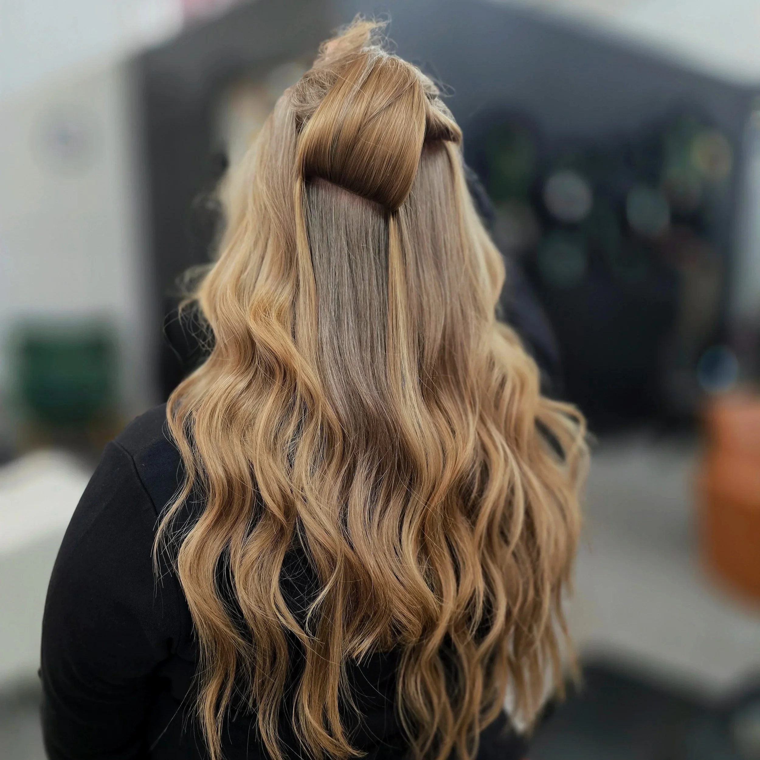 Back of a person with long, wavy, ombre hair, transitioning from light blonde to darker blonde, with a section of straightened hair clipped up.