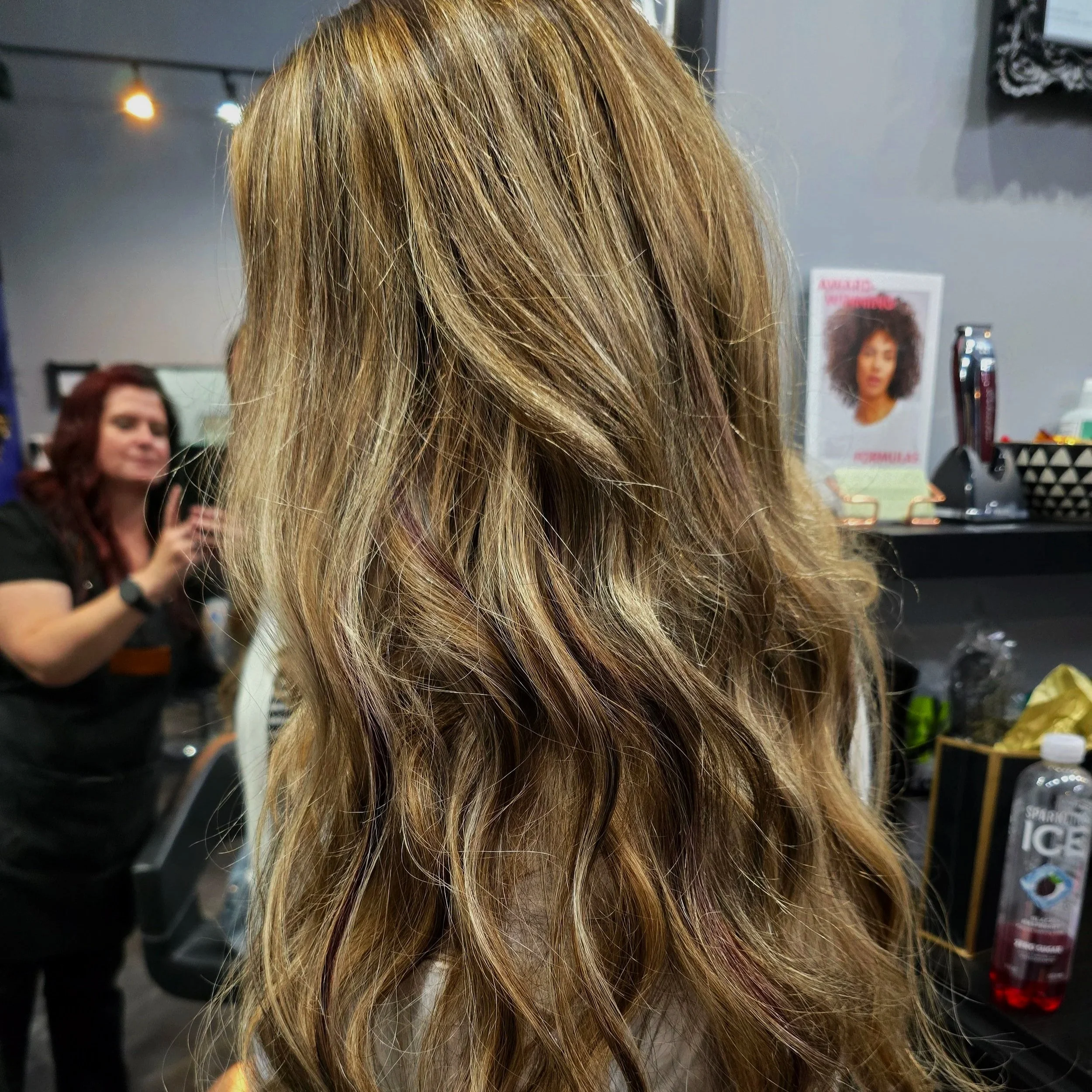 Close-up of a woman with long, wavy blonde hair with darker lowlights at a hair salon.