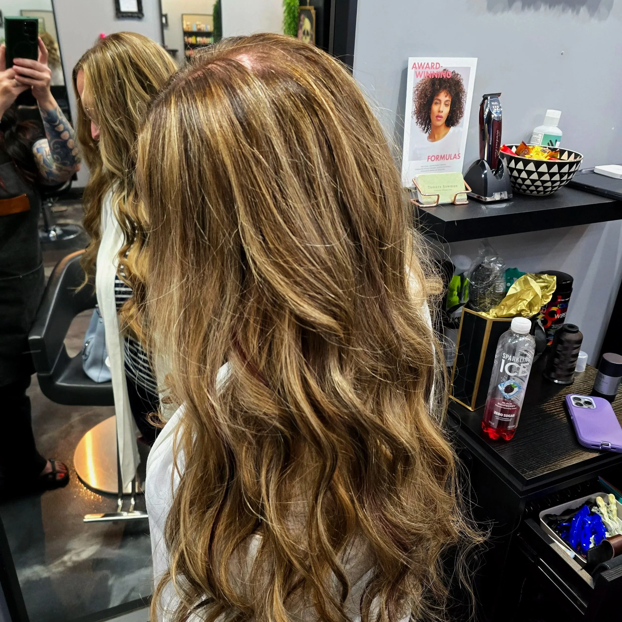Woman with long, wavy, light brown hair with highlights sitting in a salon.