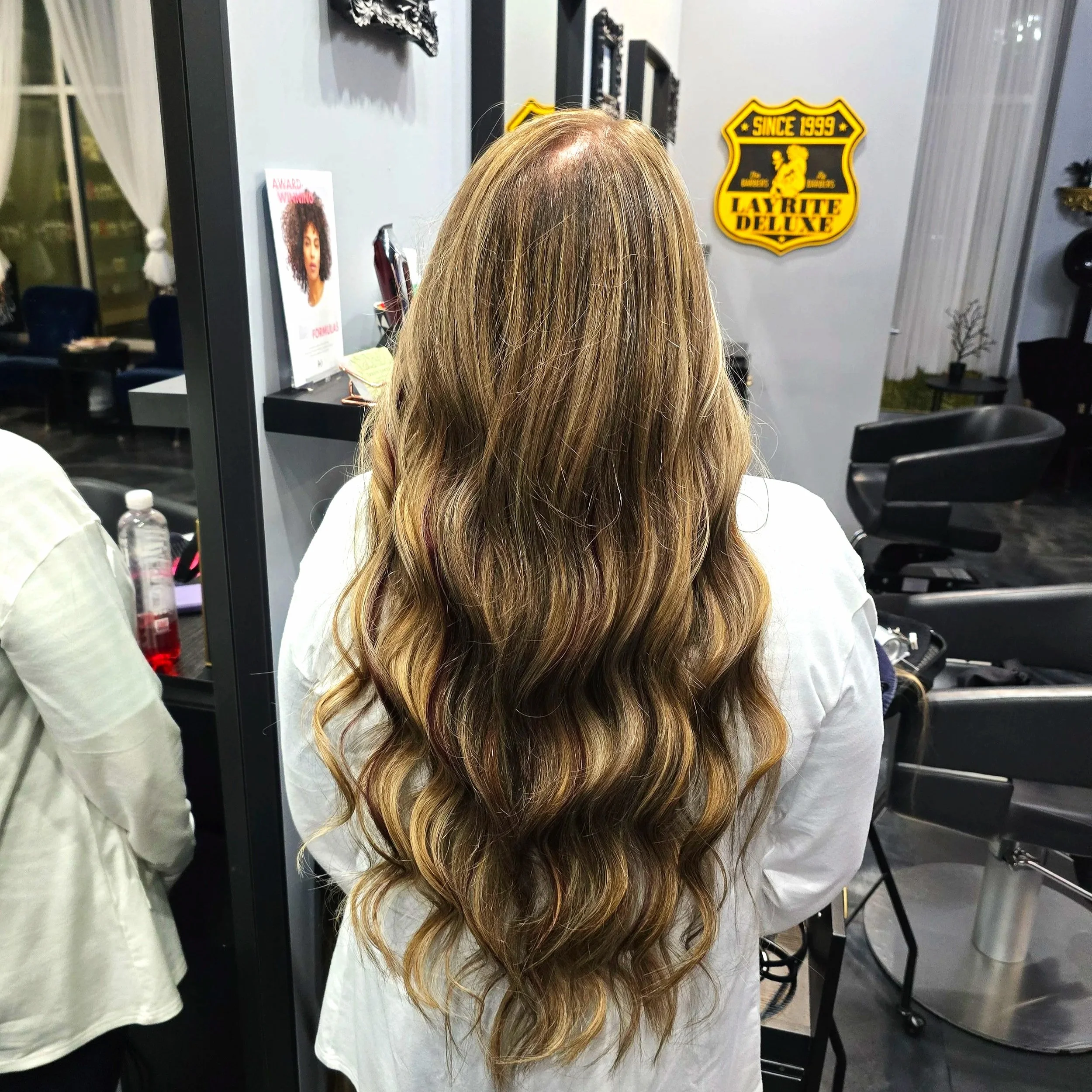 Back of a woman with long, wavy, brown hair with highlights, sitting in a hair salon.
