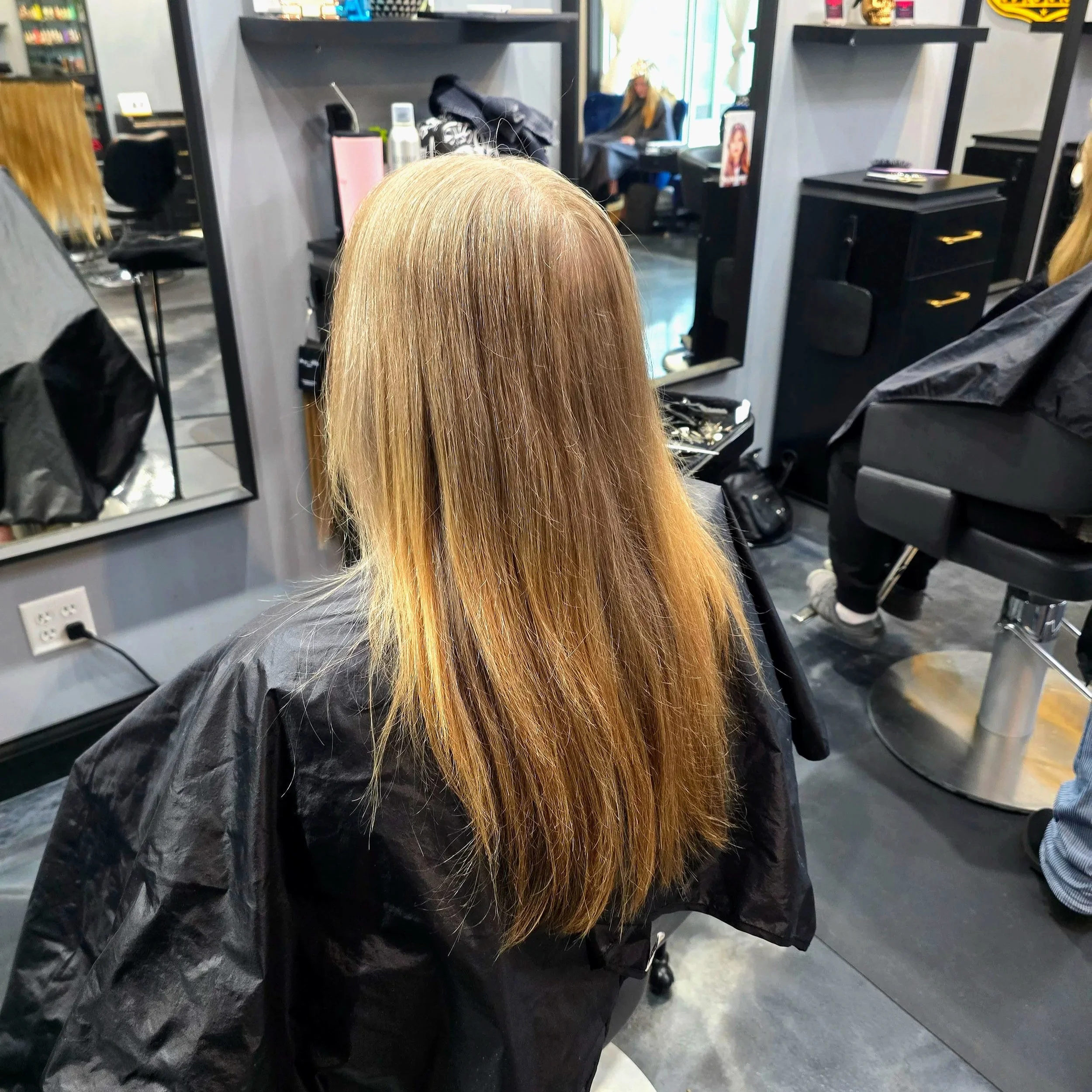 Blonde woman at a hair salon sitting in a black salon cape with her hair down, getting a haircut or styling.