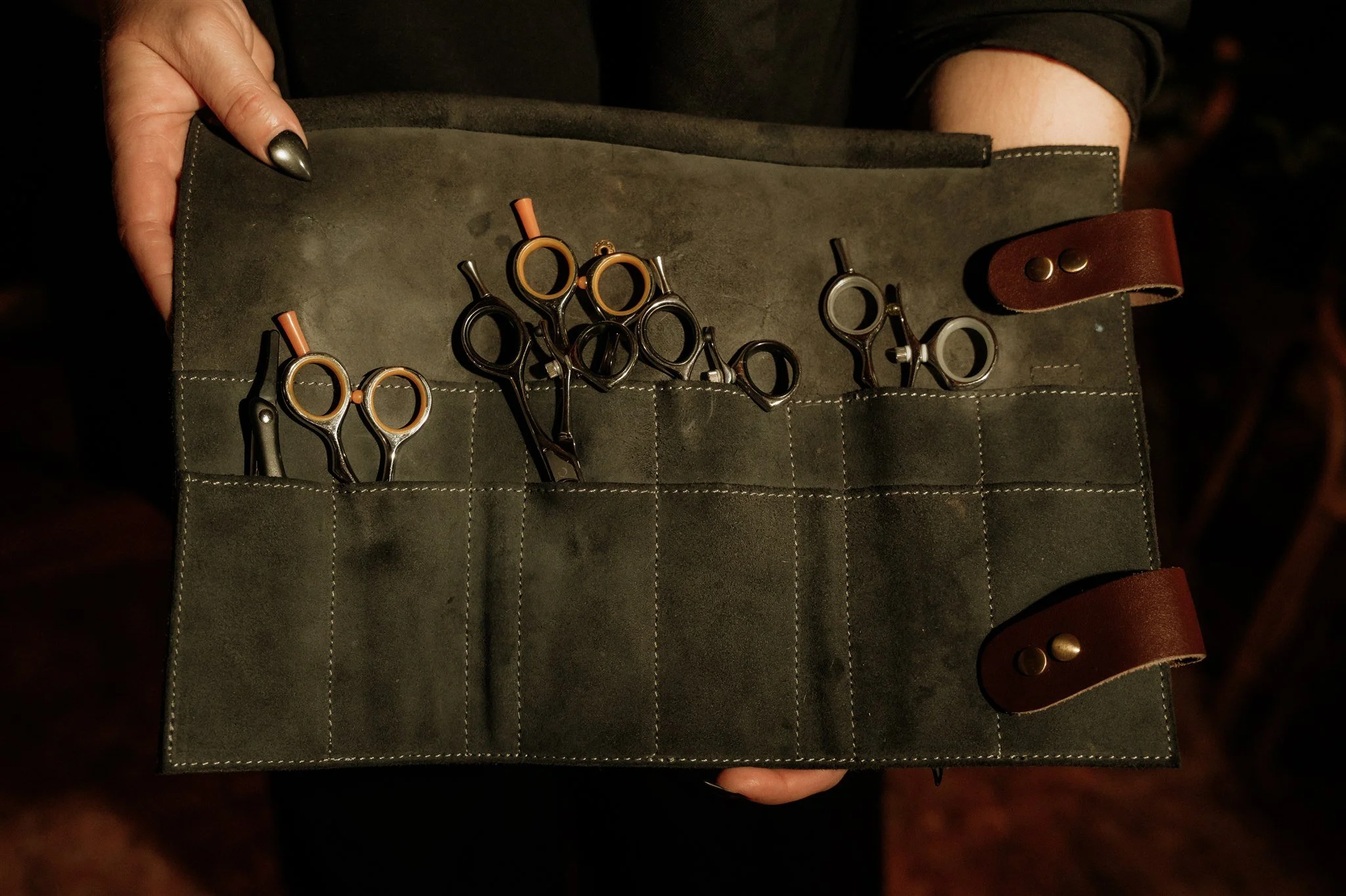 A person holding a green leather case with small scissors inside.