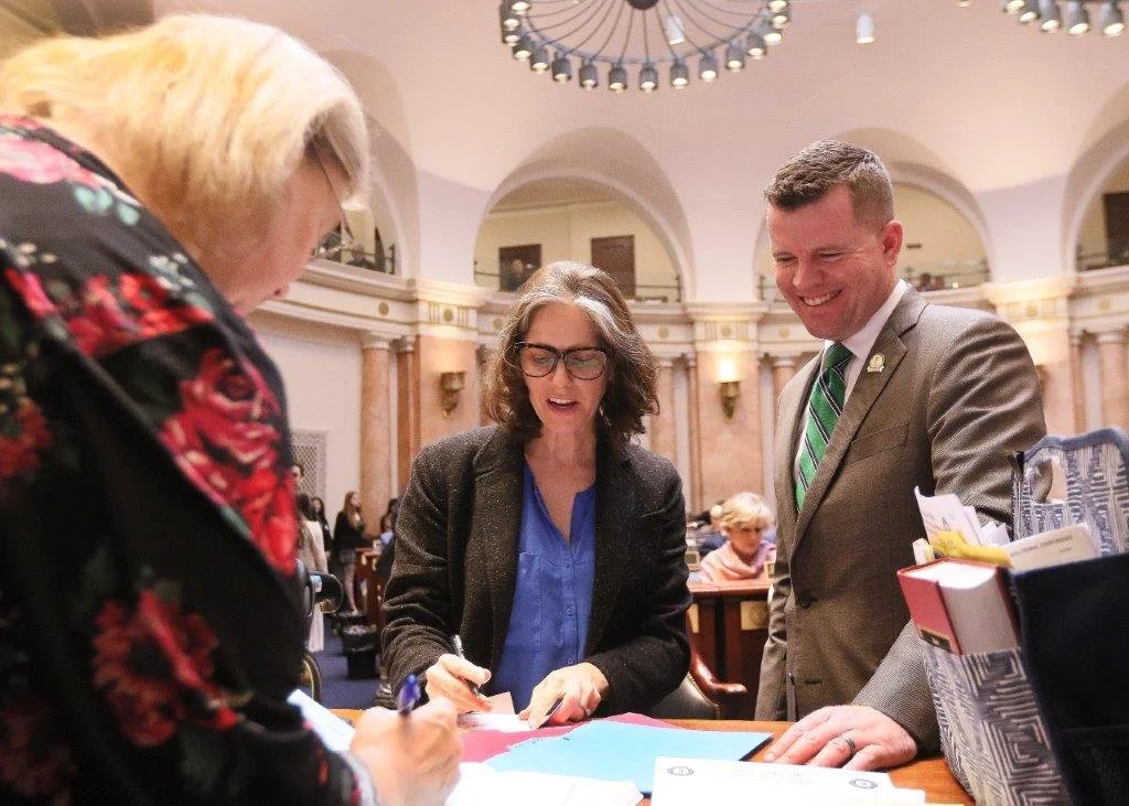 Sarah Stalker (D, KY 34) and Rep. Lewis (R, KY 90) in the Kentucky state capitol looking at documents, with another woman partially visible.