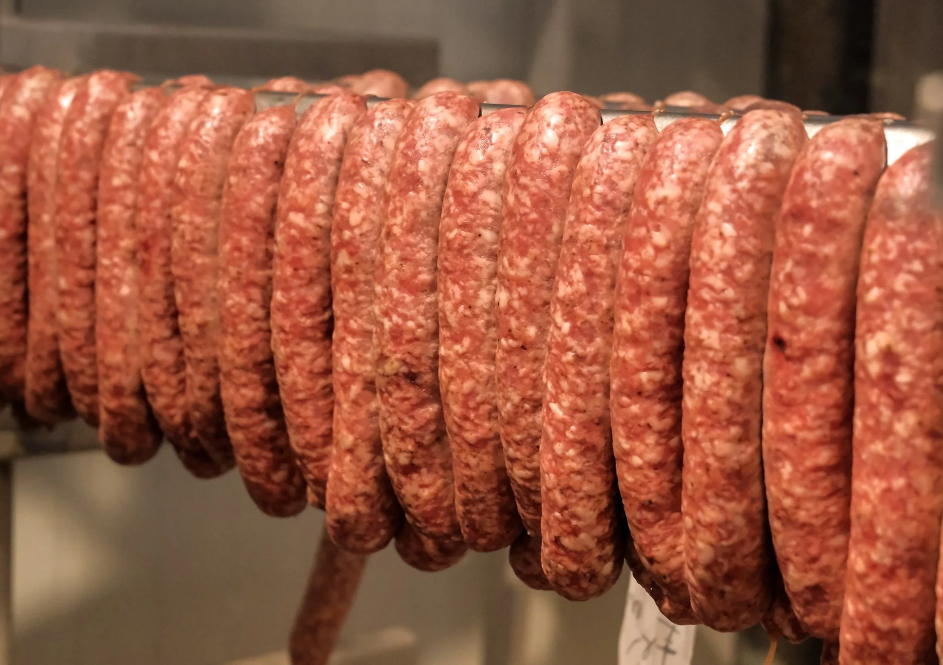Close-up of raw sausage links hanging on a rod in a meat shop or butcher's shop.