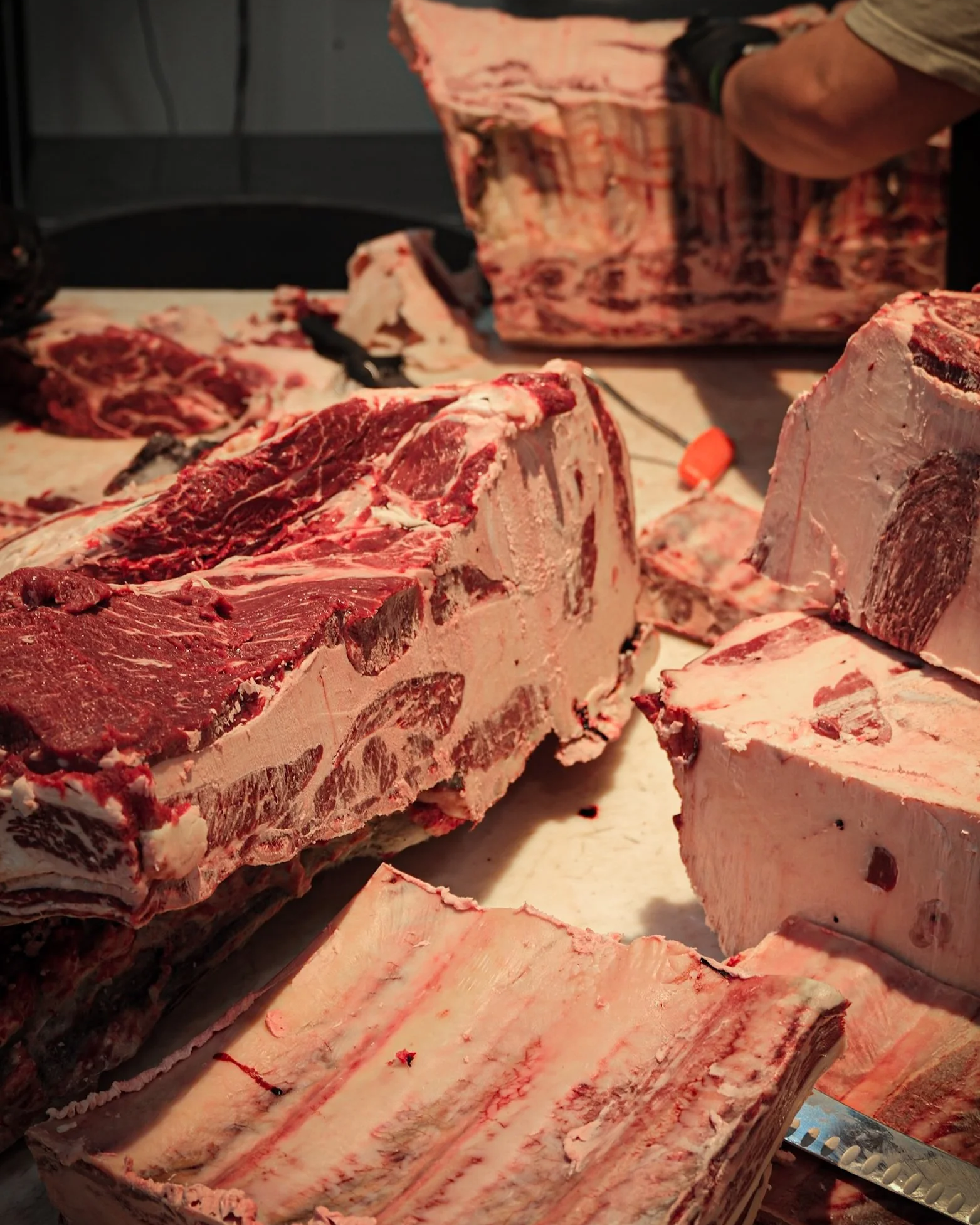 Various cuts of beef and other meat cuts on a butcher's display, with a meat saw in the background.