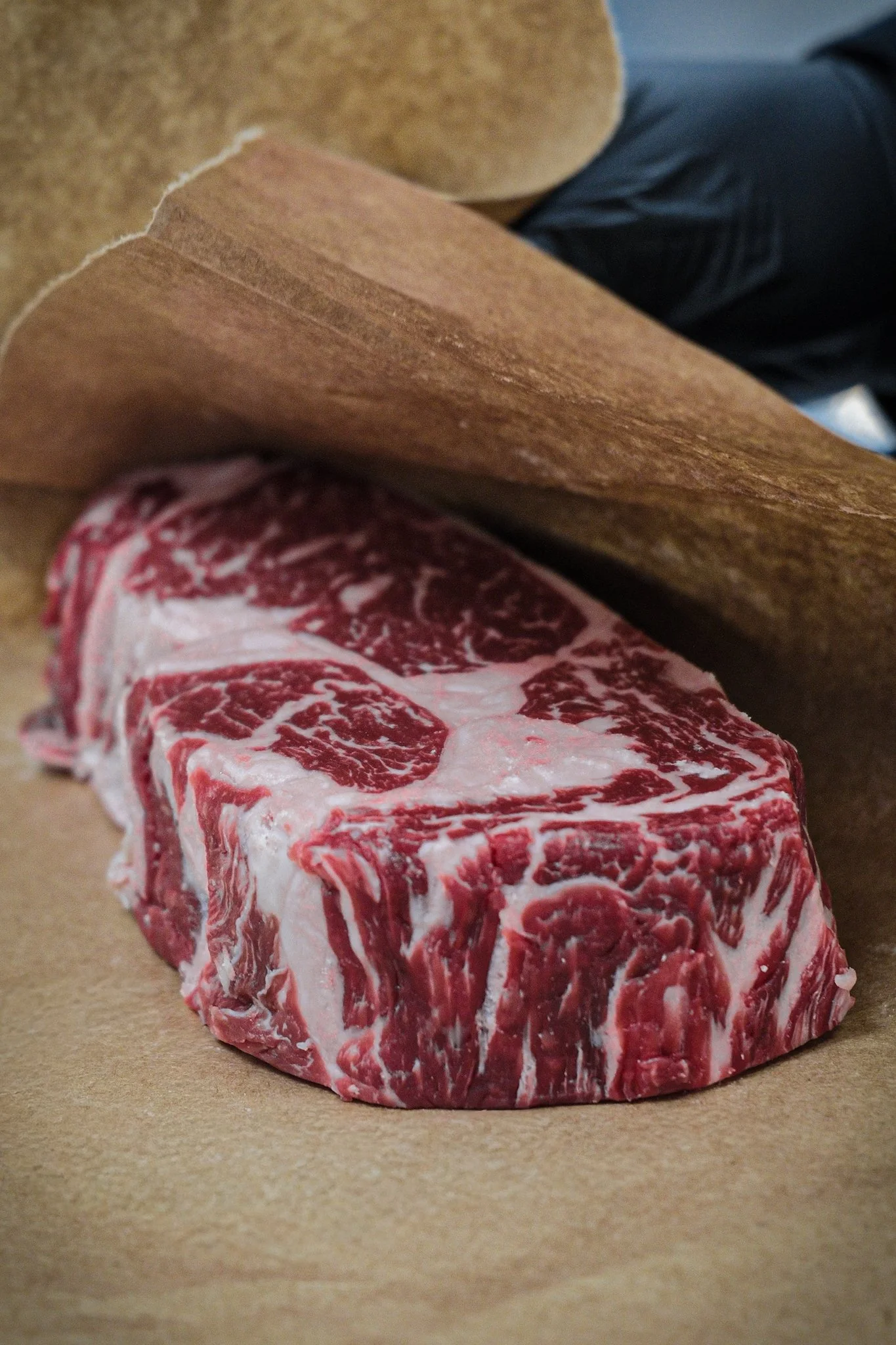 A raw beef steak with marbling, resting on a piece of brown paper or parchment.