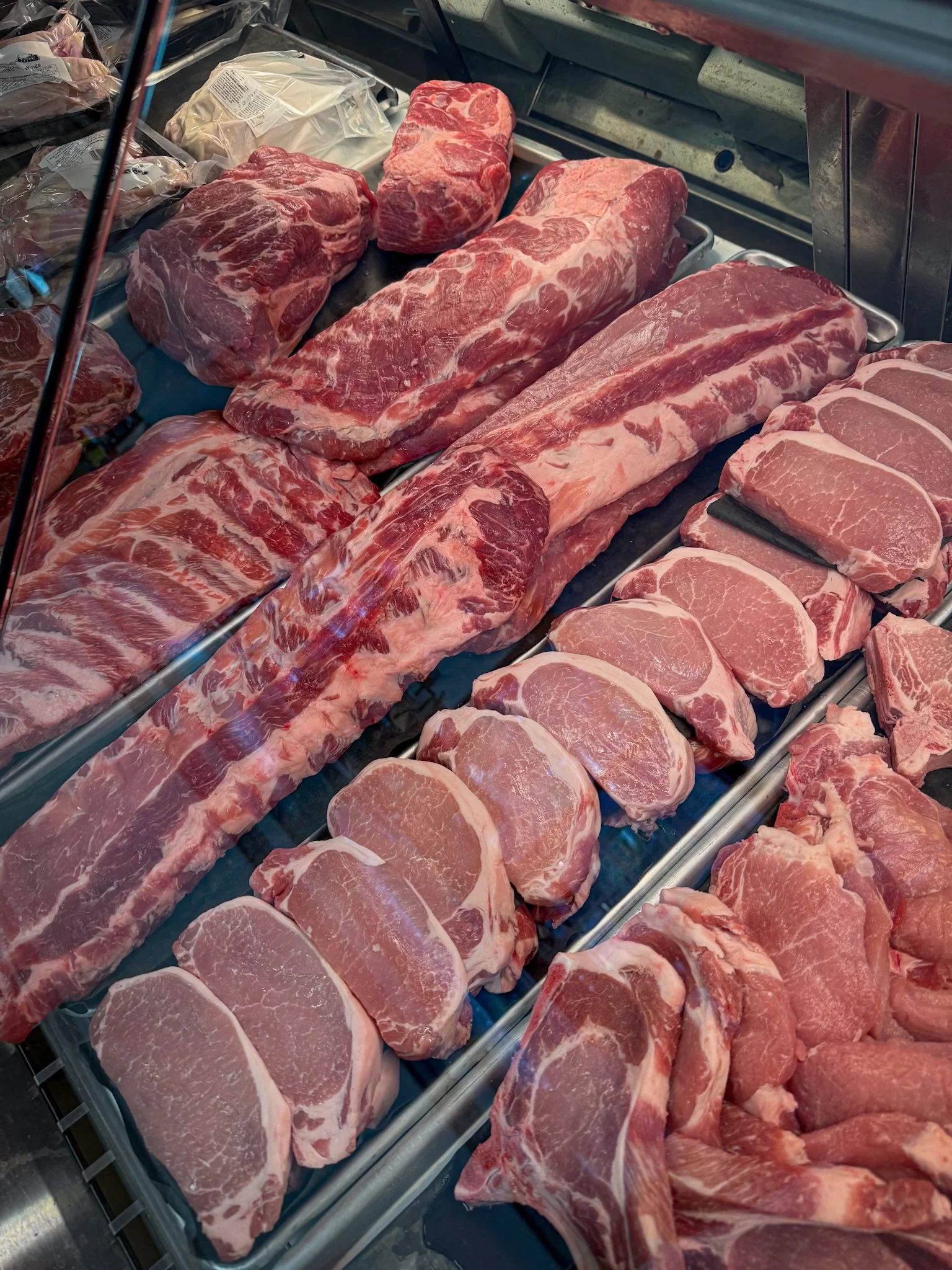 Display case filled with various cuts of fresh raw beef, including steaks and roasts.